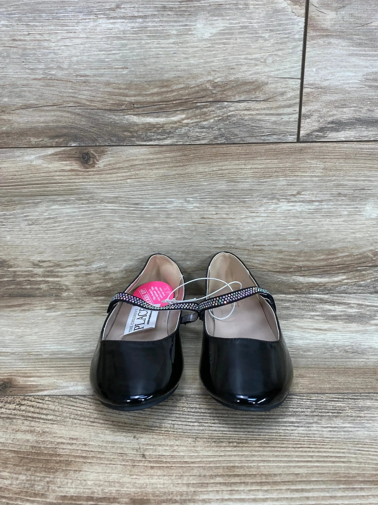 Side view of pair of black girls’ faux patent leather ballet flats showing jeweled bow detail on white background