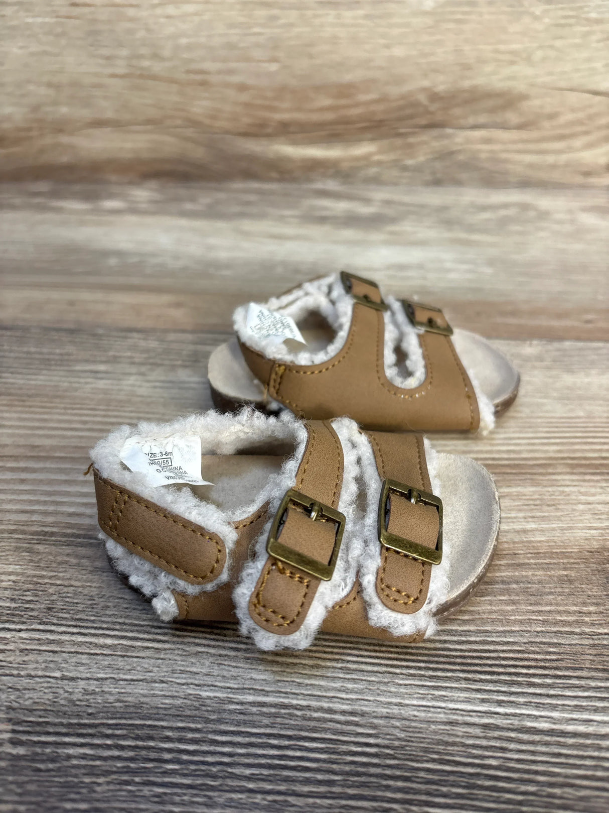 Tan baby sandals with faux fur lining and double buckle straps on wood background