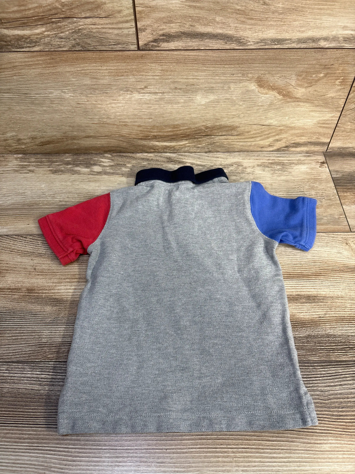 Back view of Baby Gap x Disney Mickey Mouse pique polo shirt showcasing gray fabric with red and blue sleeves on wood flooring
