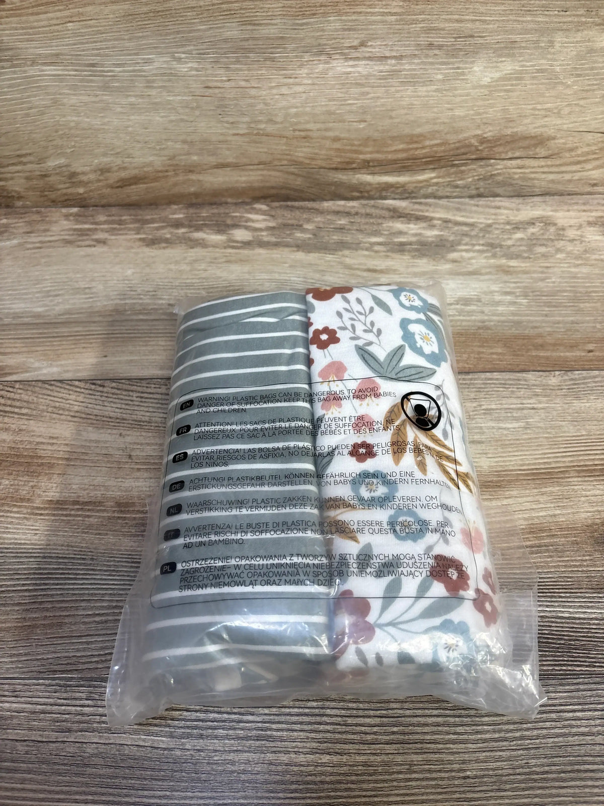 Front view of Momcozy 2-pack swaddle blankets showing gray stripes and floral print in clear packaging on light wood