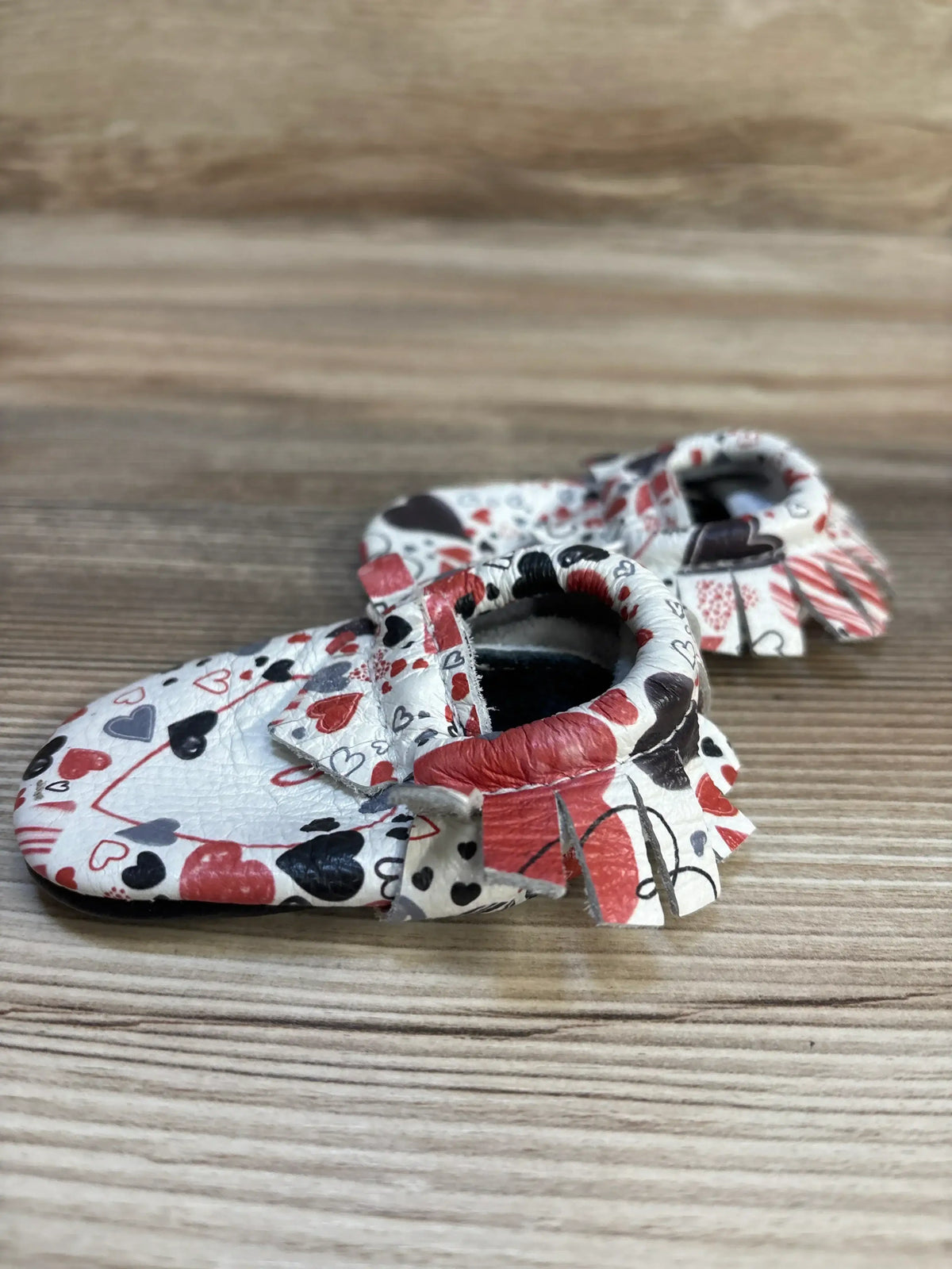 Baby moccasins with red, black, and gray heart pattern on wooden background