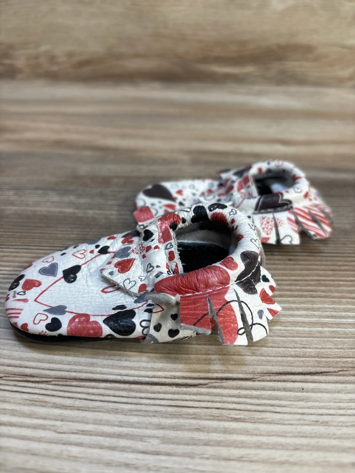 Baby moccasins with red, black, and gray heart pattern on wooden background