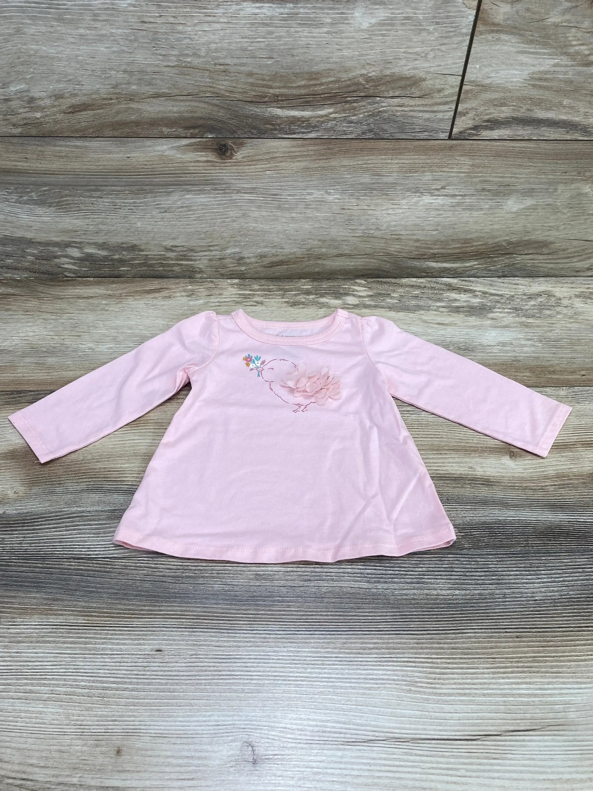 Flat-lay front of First Impressions pink long-sleeve baby birdie shirt showcasing 3D flower applique and bird embroidery on wood background