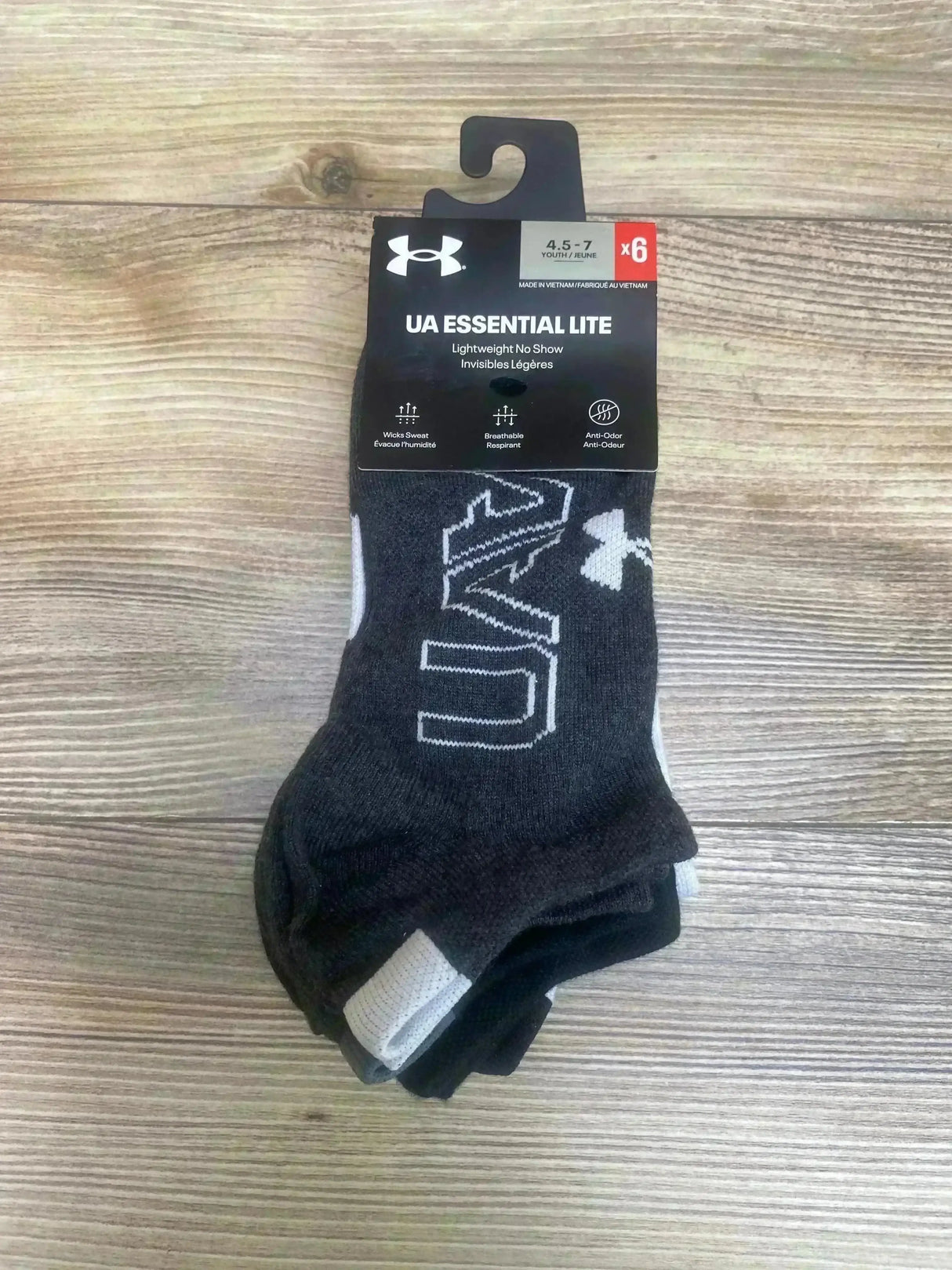 Top view of Under Armour 6-pack no-show socks, black/gray with UA logo and ‘UA Essential Lite’ label, size 4.5-7 on wood