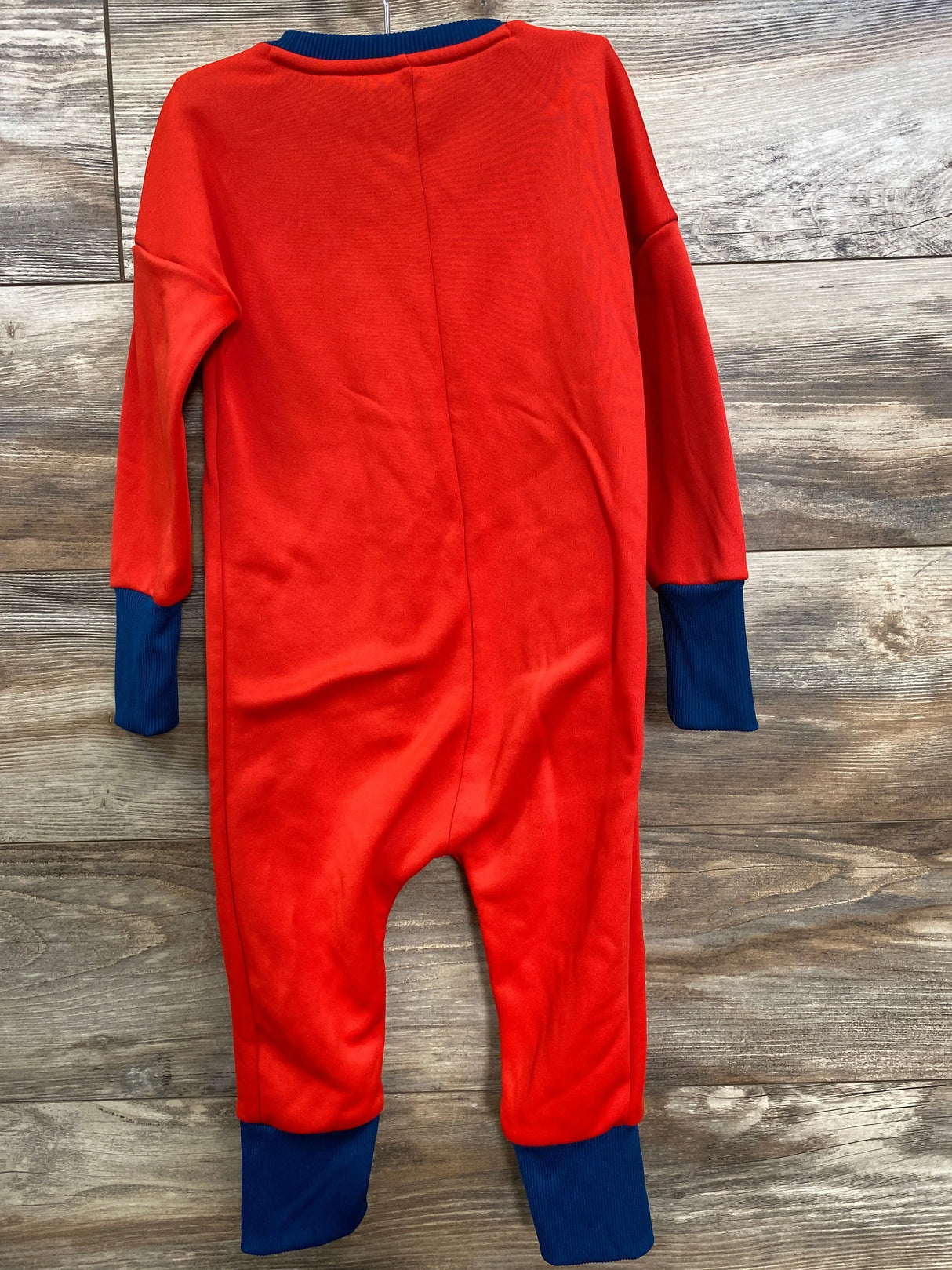 Back view of Adidas x Lego red coverall, size 2T, showing navy blue ribbed cuffs on sleeves and legs on wooden floor