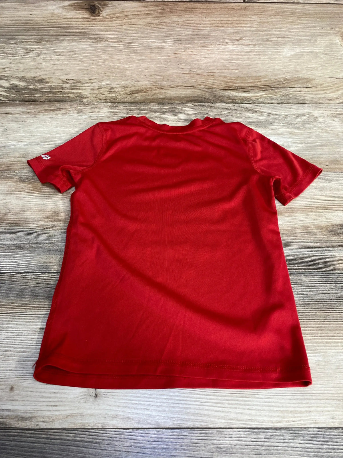 Back view of red All In Motion toddler athletic shirt (size 4-5T) showing short sleeves and small white sleeve logo on wood background