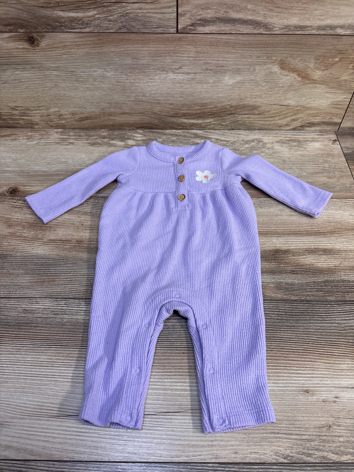 Flat lay of purple waffle knit henley coverall for 0-3 months showing wooden chest buttons, embroidered flower, and snap leg closures on wood background