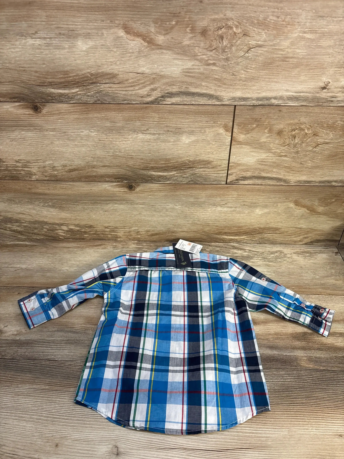 Flat-lay back view of U.S. Polo Assn. toddler button-up plaid shirt in blue and white showing long sleeves and button cuffs on wood background