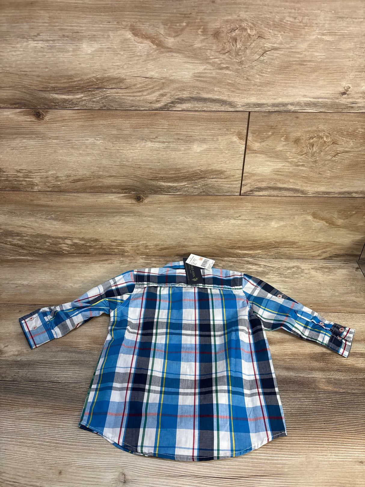 Flat-lay back view of U.S. Polo Assn. toddler button-up plaid shirt in blue and white showing long sleeves and button cuffs on wood background
