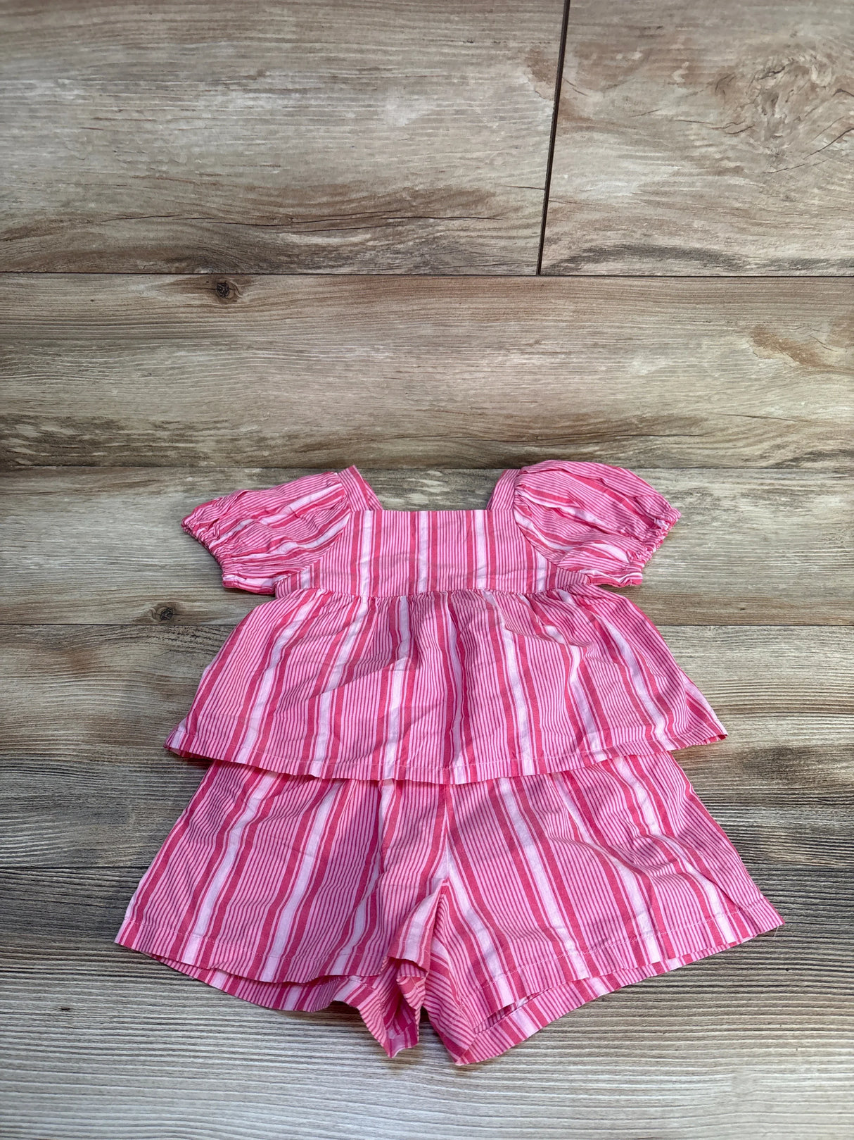 Flat-lay of Baby Gap pink and white striped 2-piece set with puff-sleeve peplum top and elastic-waist shorts on wood