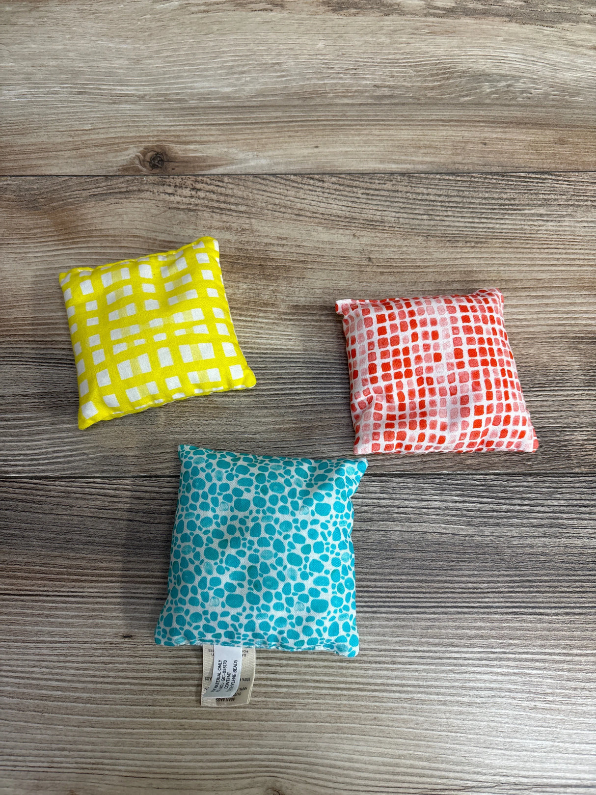 Three small colorful fabric bean bags with yellow, red, and blue patterned designs on rustic wooden surface