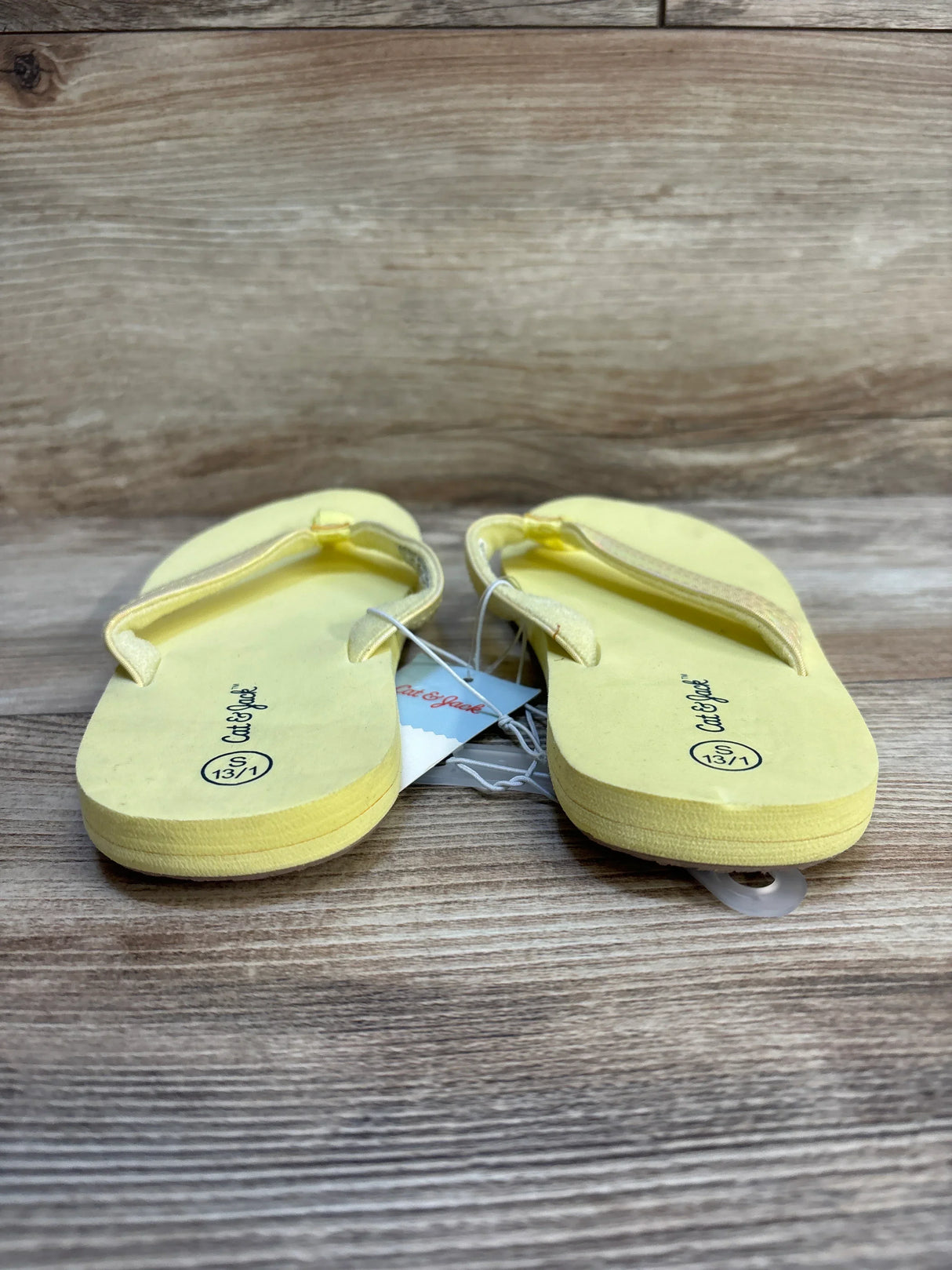 Yellow children's flip flops size 13/1 on wood background, casual kids sandals
