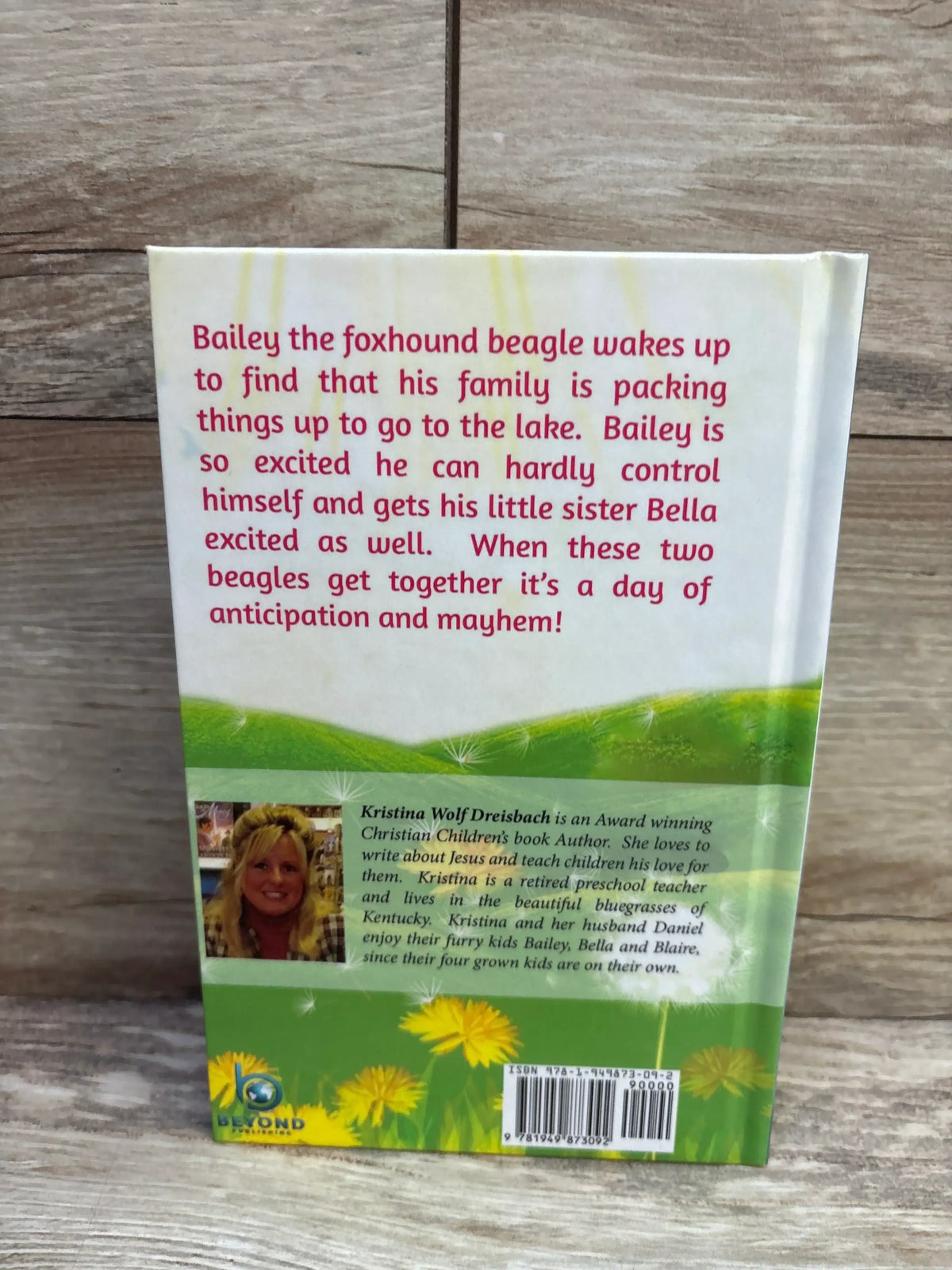 Back of hardcover book 'A Tale From A Fox Hound Beagle Named Bailey' showing red synopsis, author photo, barcode on wood