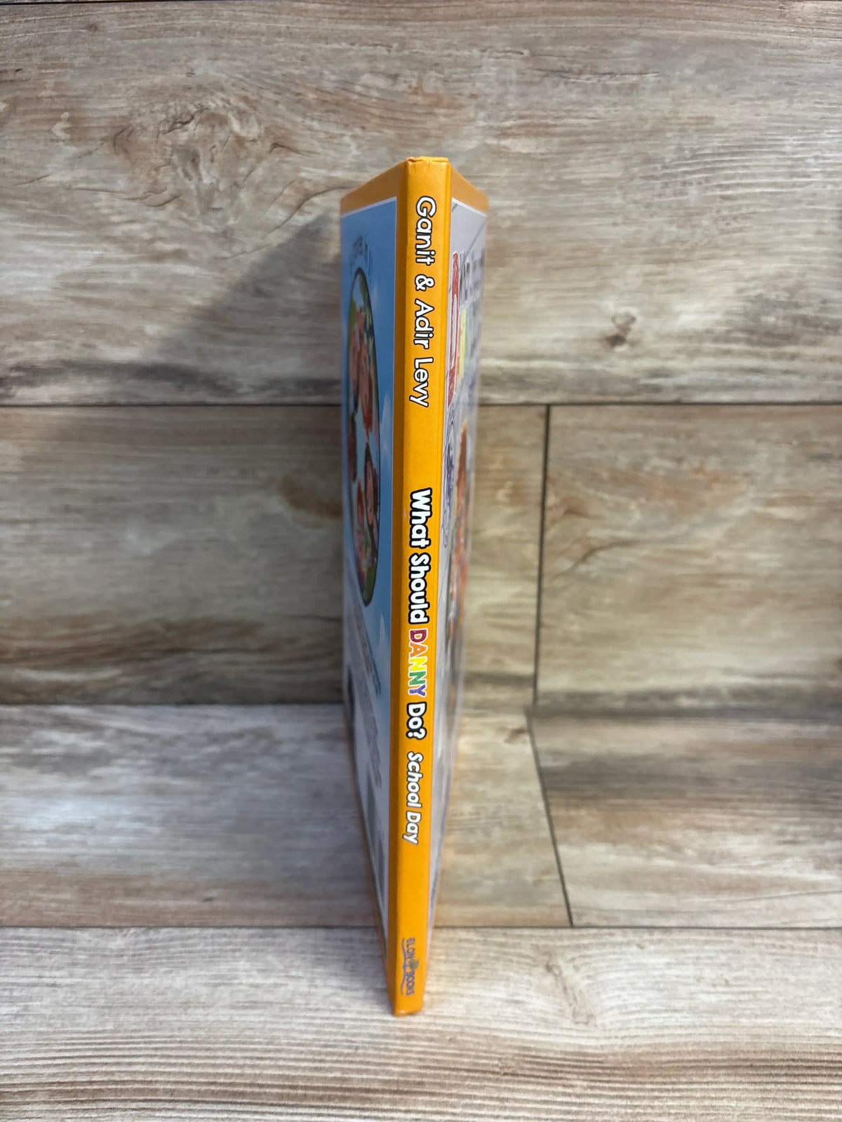 Side view of What Should Danny Do? School Day hardcover book by Ganit and Adir Levy, showing yellow spine on wood surface