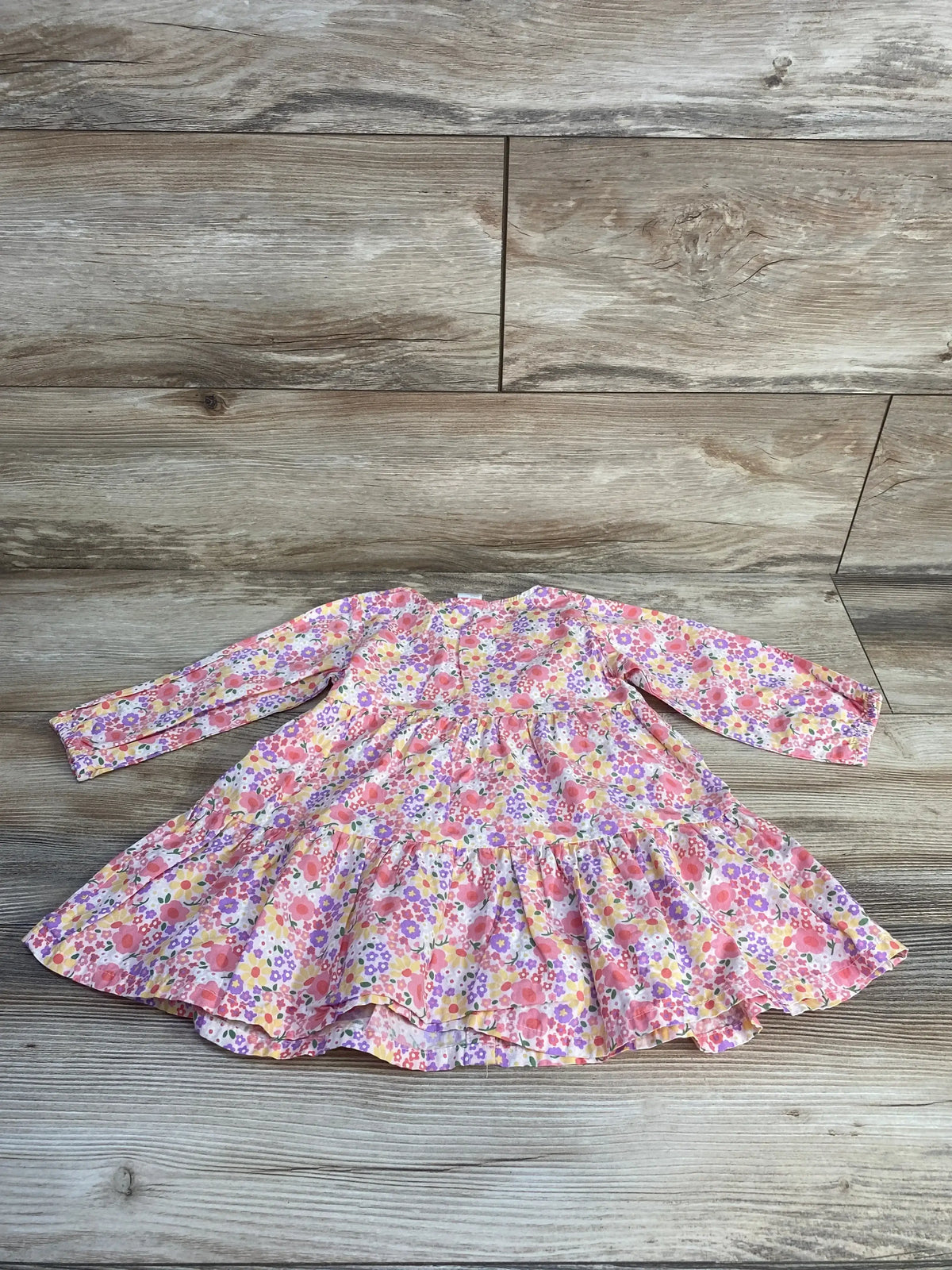 Front view of H&M pink floral button-front baby dress (9 months) showing gathered waist and wooden buttons on white background