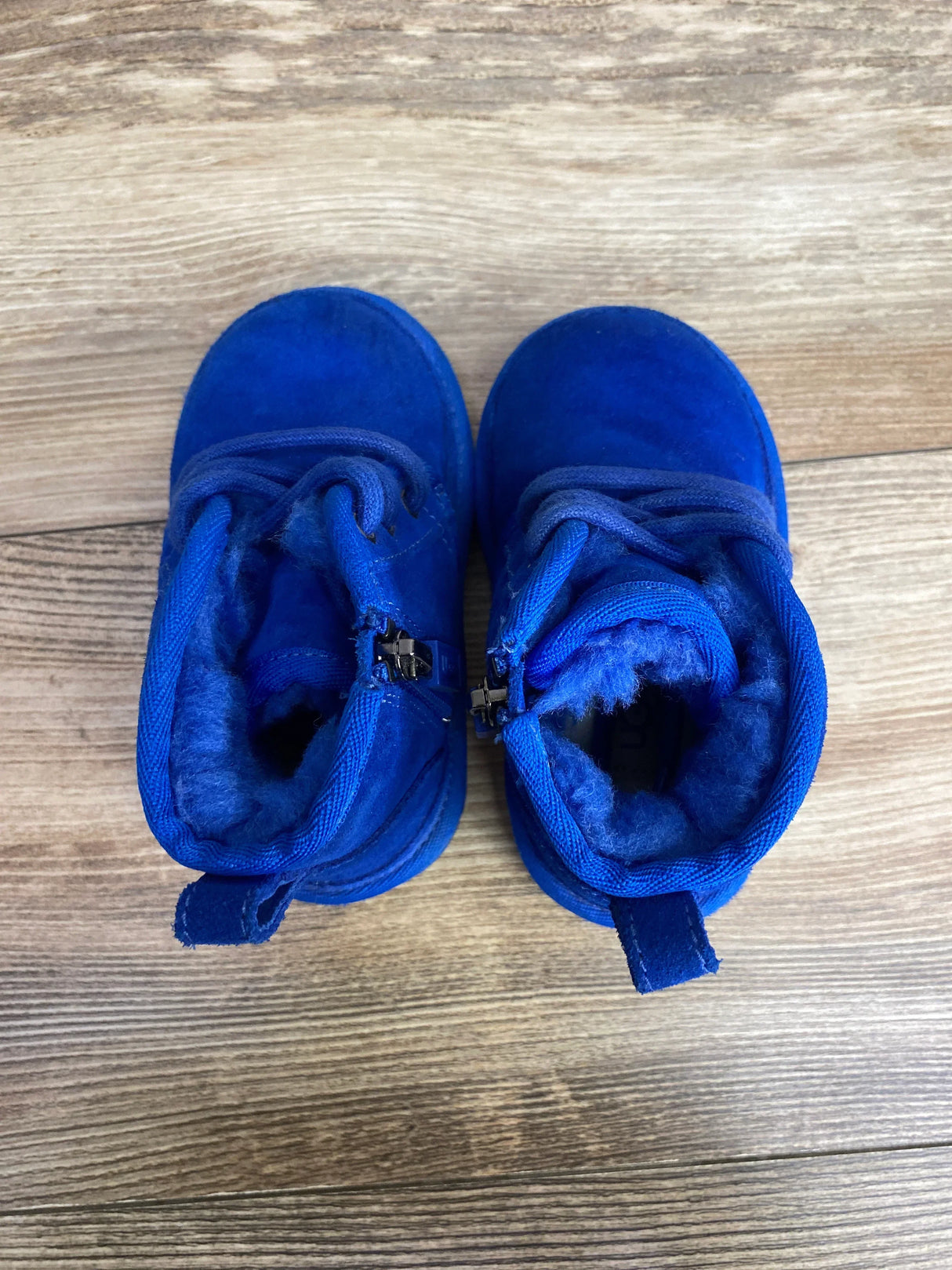 Top view of Ugg Neumel II toddler boots, bright blue, showing fuzzy shearling lining, side zippers and laces on wooden floor