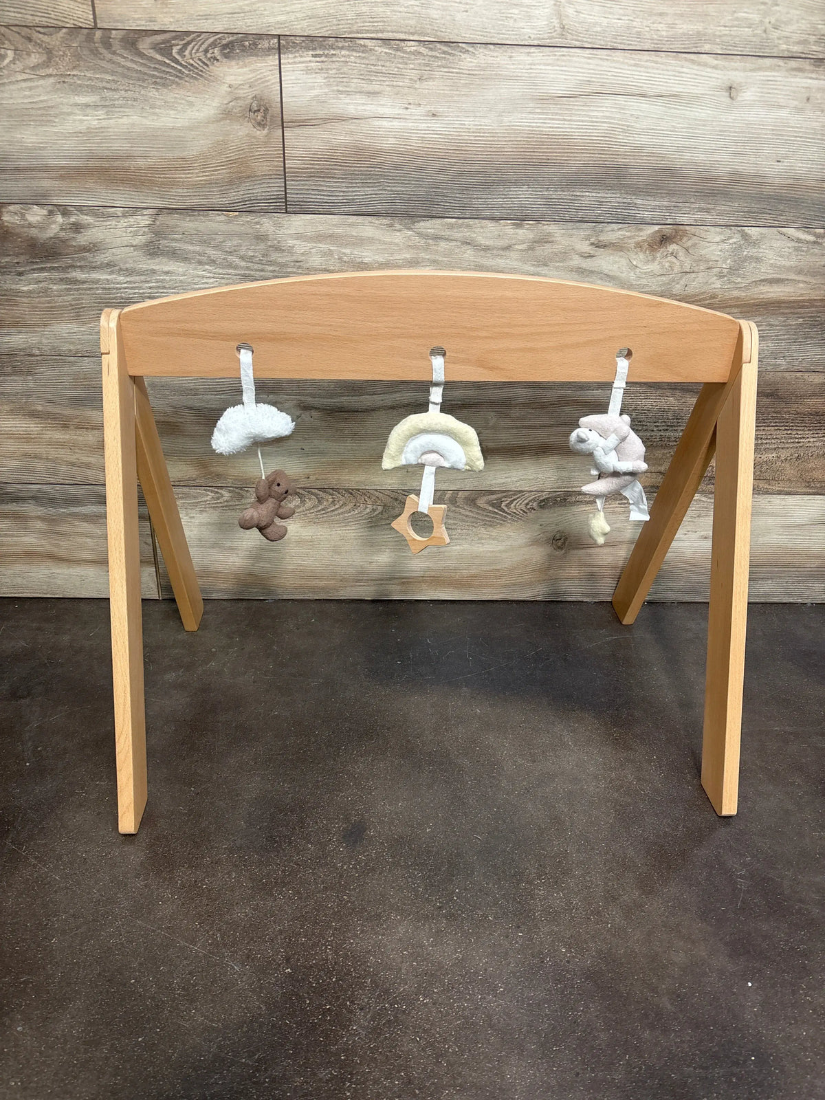 Front view of Pottery Barn Kids Wooden Activity Gym with one wooden arch and three hanging toys against wood-grain wall