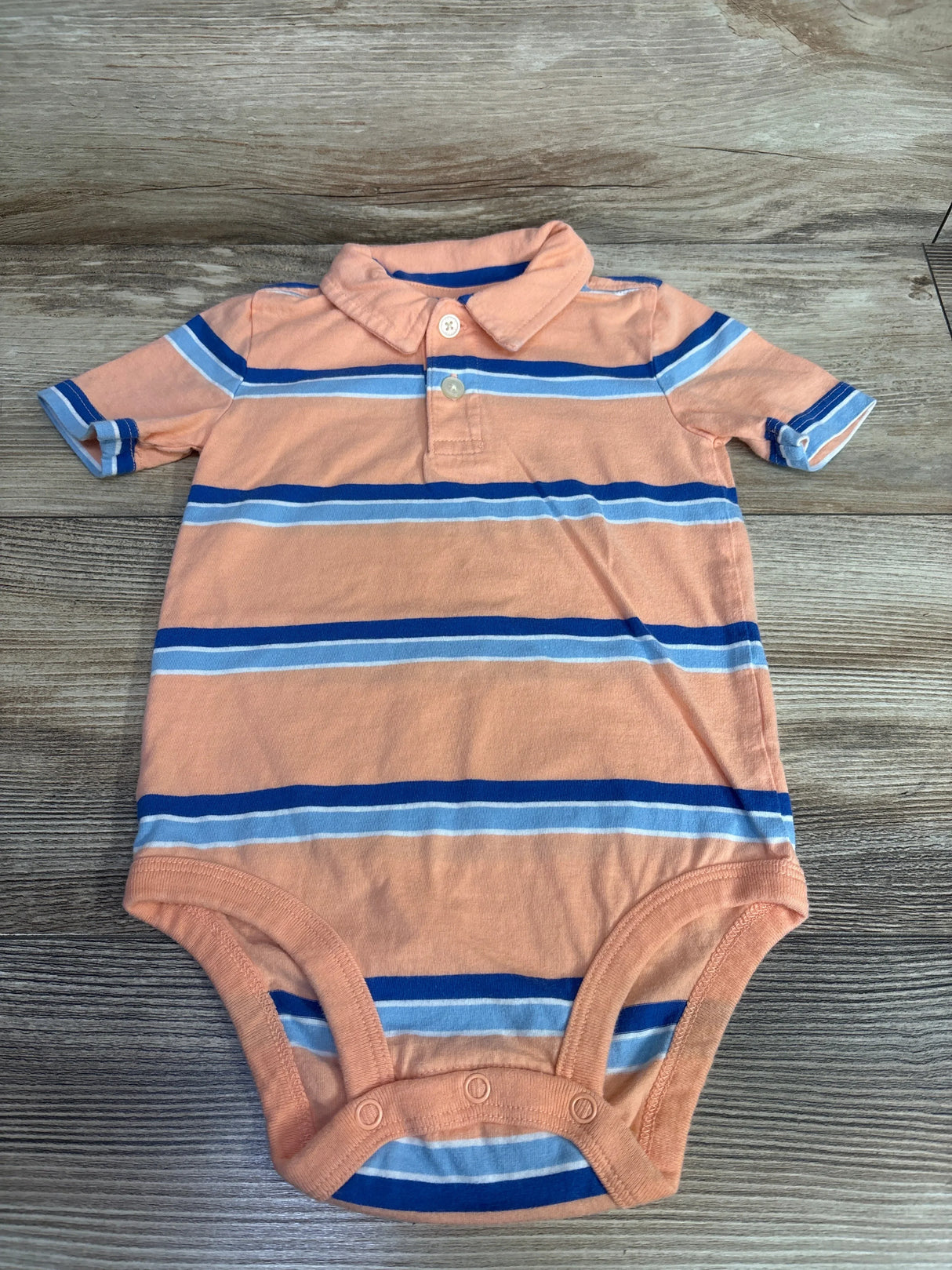Peach and blue striped short-sleeve baby onesie with collar and snap closure, laid on wooden surface