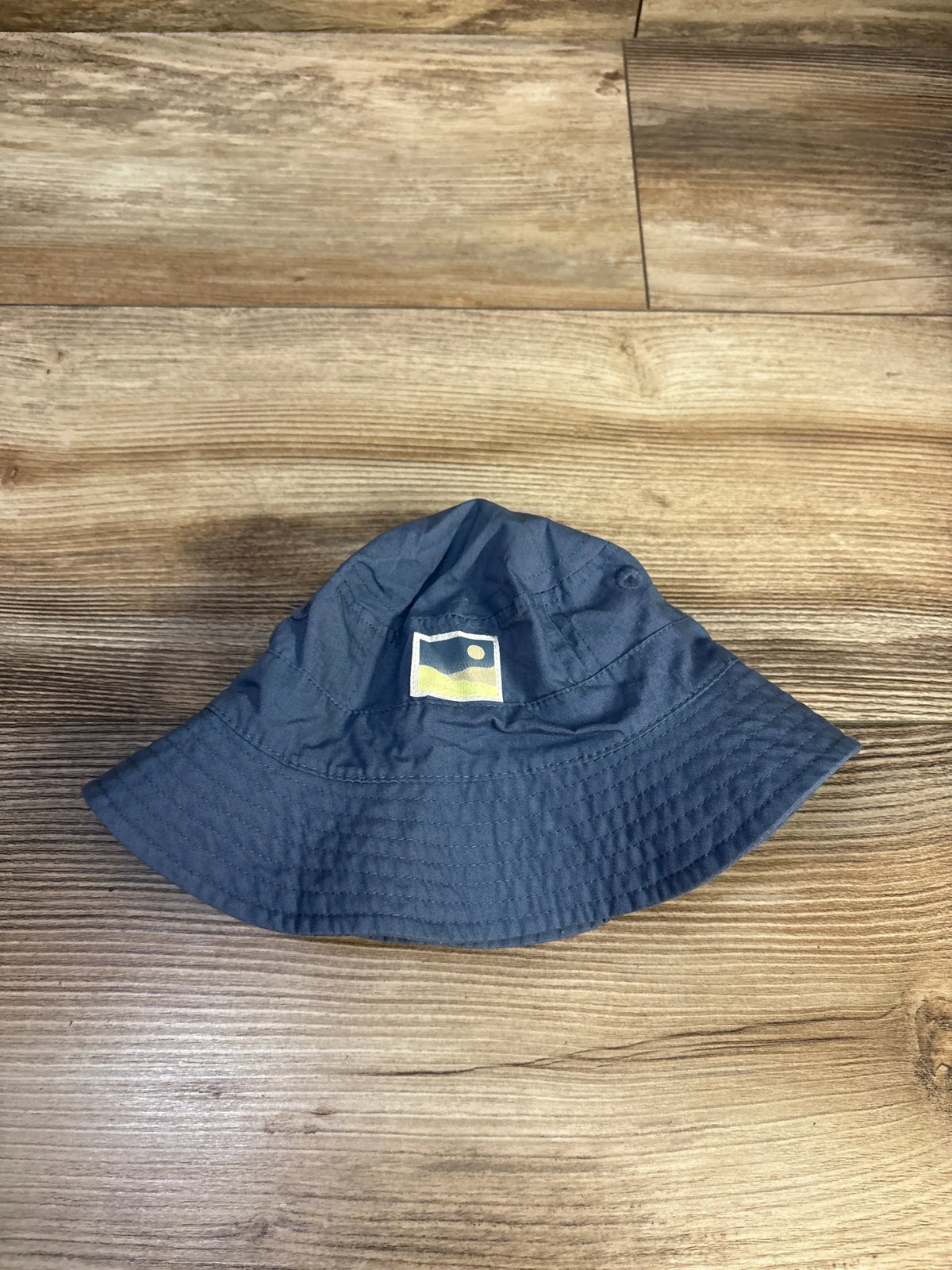 Overhead view of Carter’s blue bucket hat for 0 to 3 months showcasing its stitched brim on a wood floor