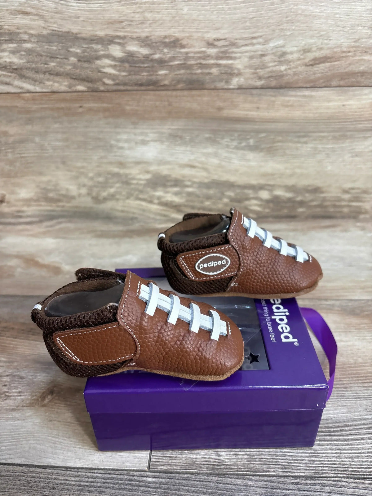 Brown leather baby shoes with white laces on a purple Pediped box on wooden surface