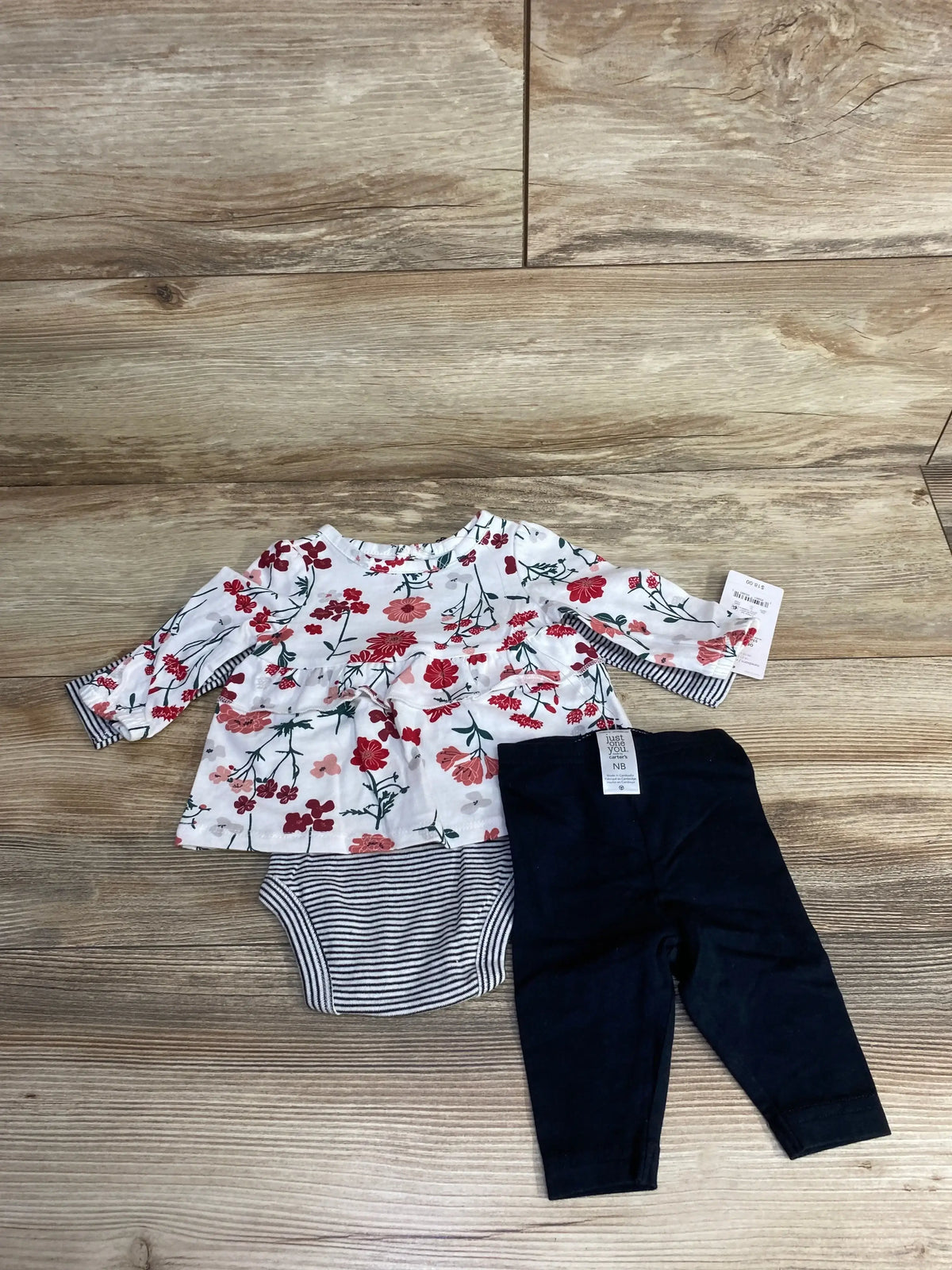 Newborn girl outfit with floral top, striped bodysuit and black leggings on wood floor