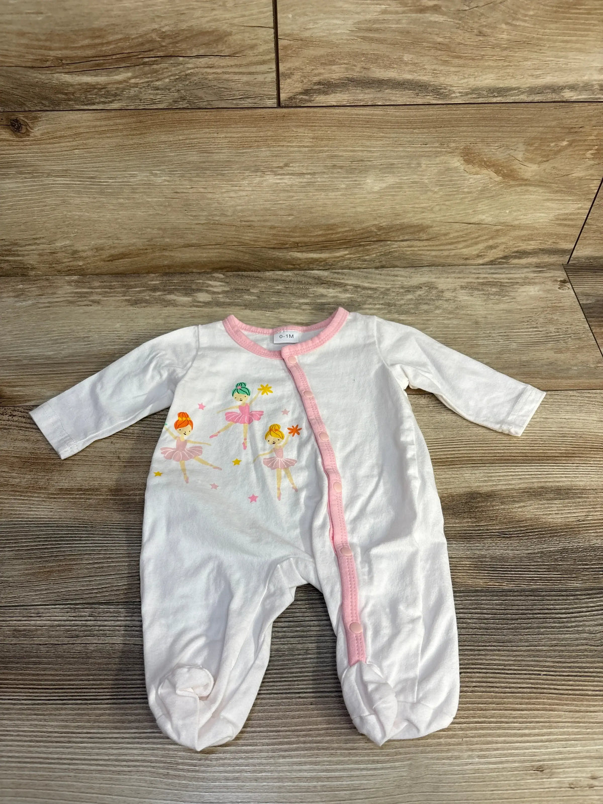 Top-down view of white baby sleeper (0-1M) showcasing pink trim, ballerina graphic, front snap closure and covered feet on wood floor