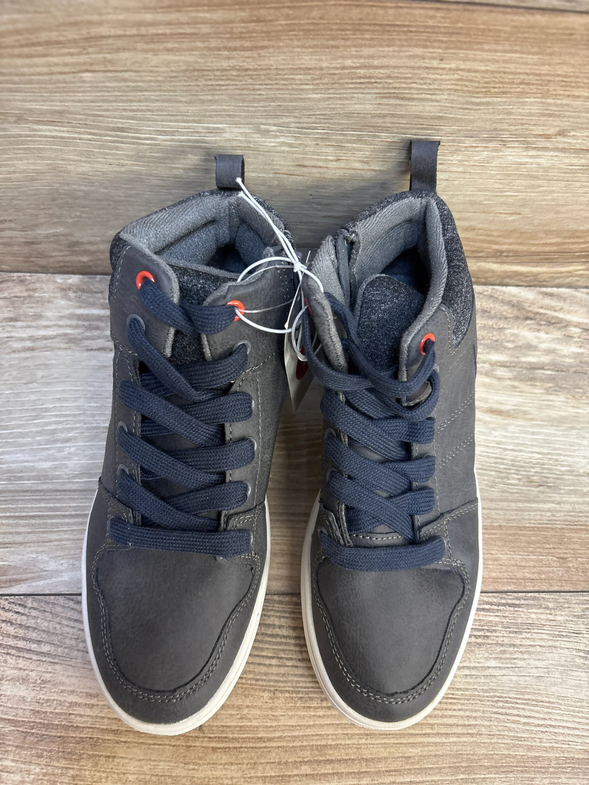 Pair of dark gray high-top kids sneakers with navy laces on wooden floor