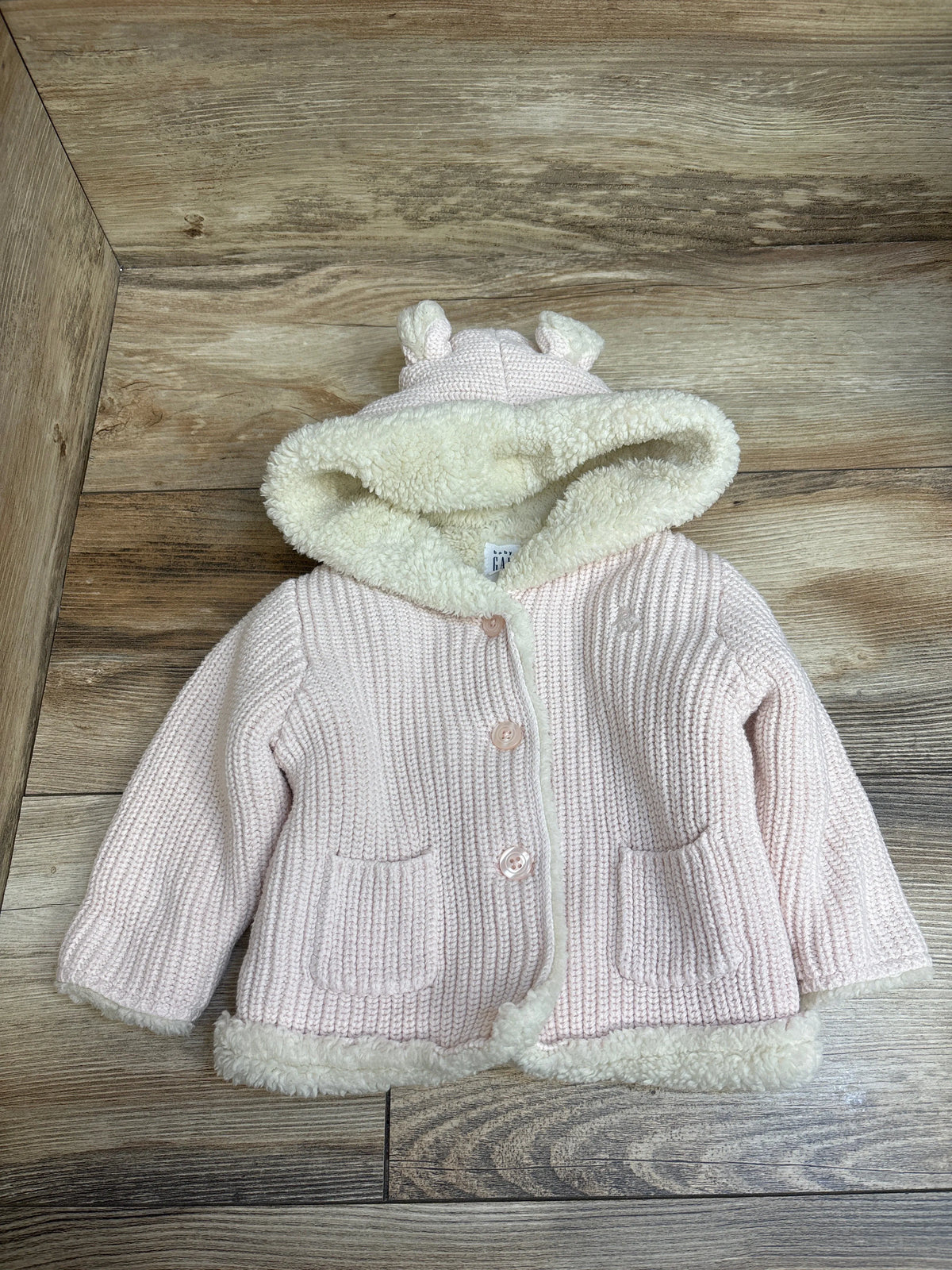 Front view of Baby Gap pink lined knit bear cardigan showcasing sherpa lining, bear-ear hood, and pockets on a wood floor