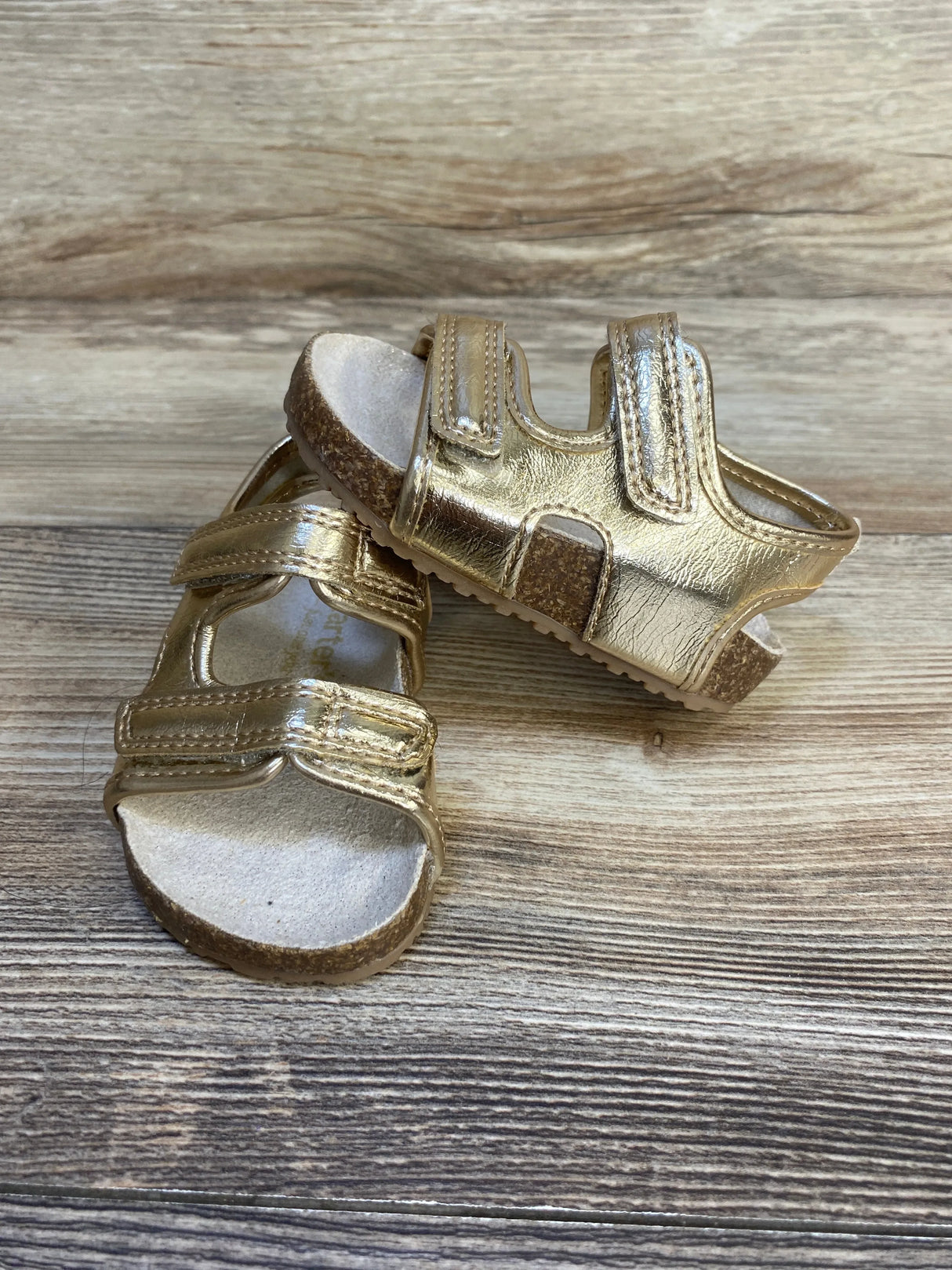 Gold toddler sandals with cork soles and velcro straps on wooden background