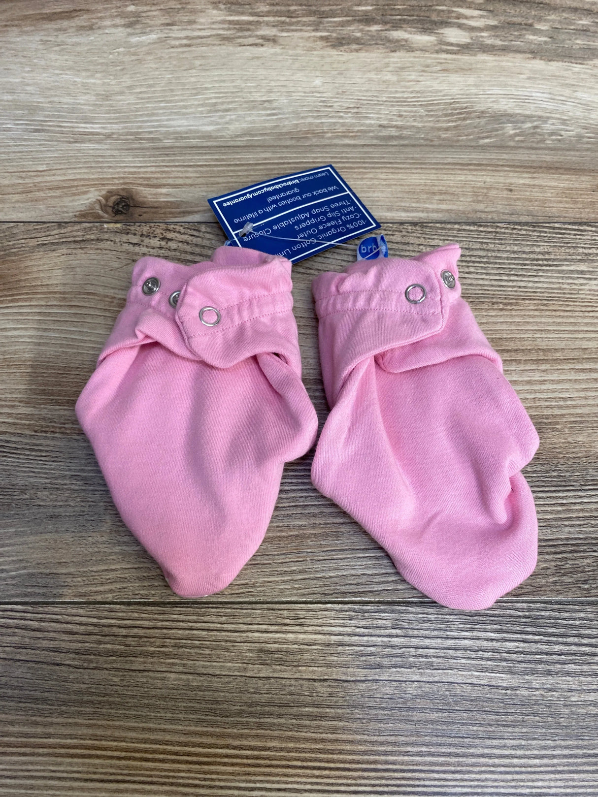 Top-down view of pink baby booties for 6-12 months showing snap-button ankle cuffs on wood background