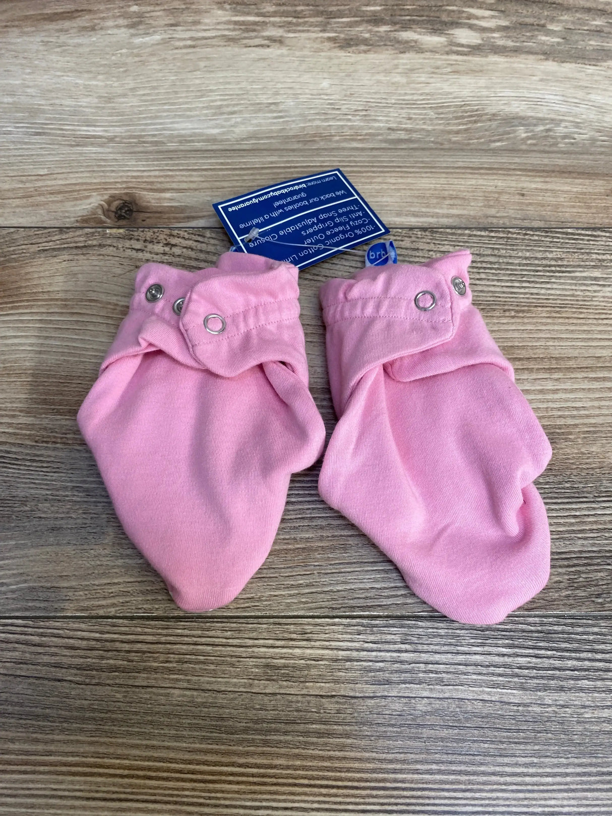 Top-down view of pink baby booties for 6-12 months showing snap-button ankle cuffs on wood background