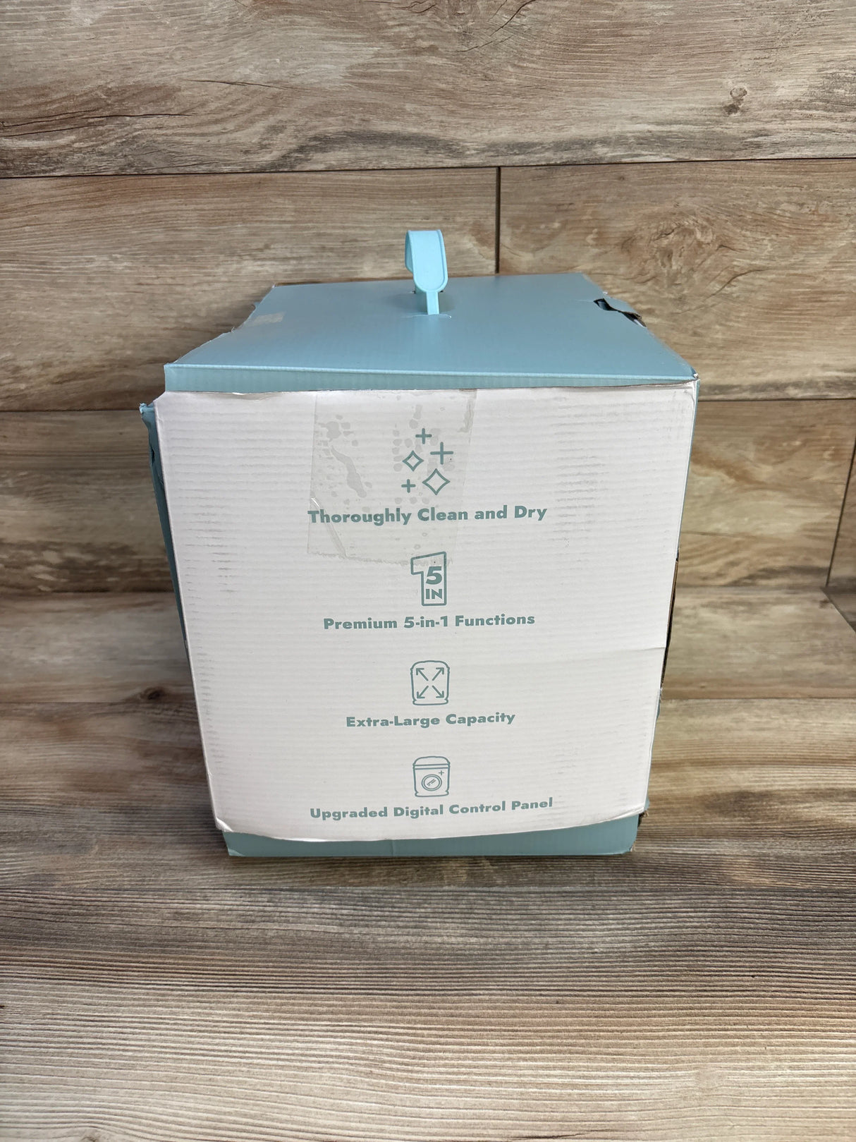 White and blue product box on wooden surface featuring text about clean dry, 5-in-1 functions, large capacity, digital control panel