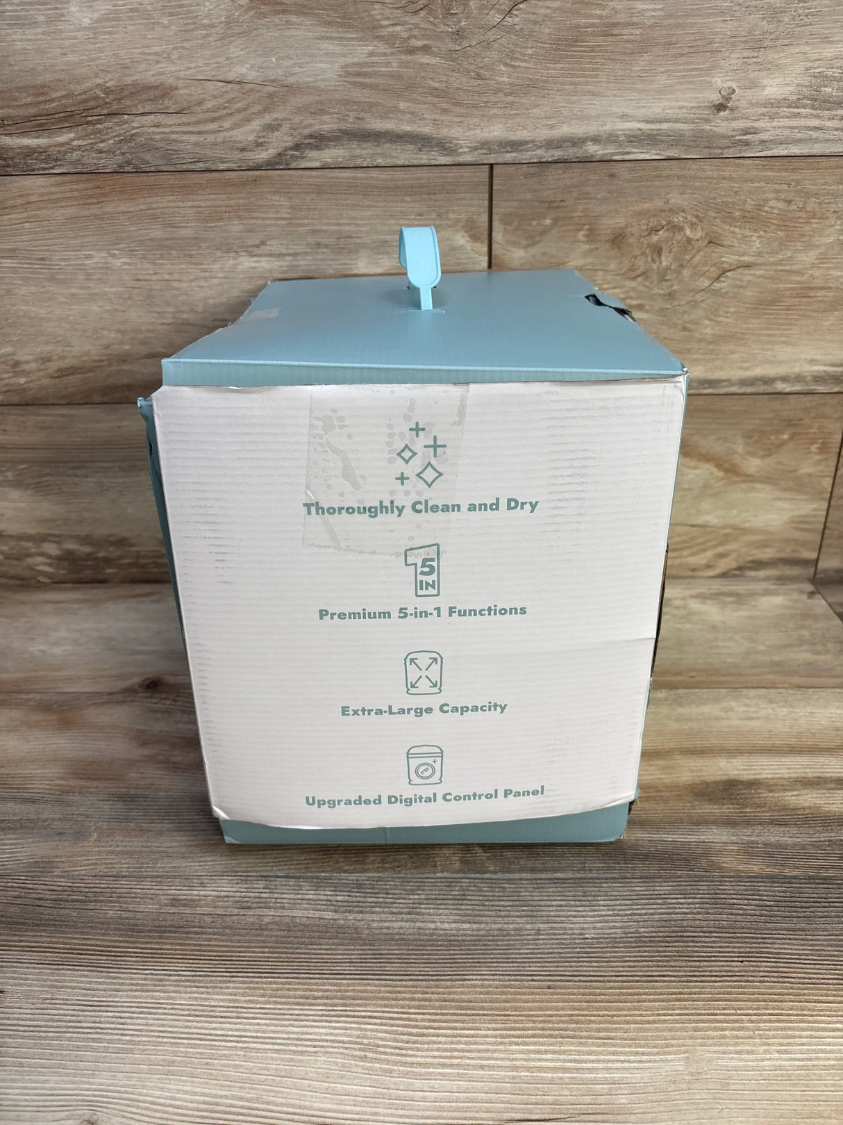 White and blue product box on wooden surface featuring text about clean dry, 5-in-1 functions, large capacity, digital control panel