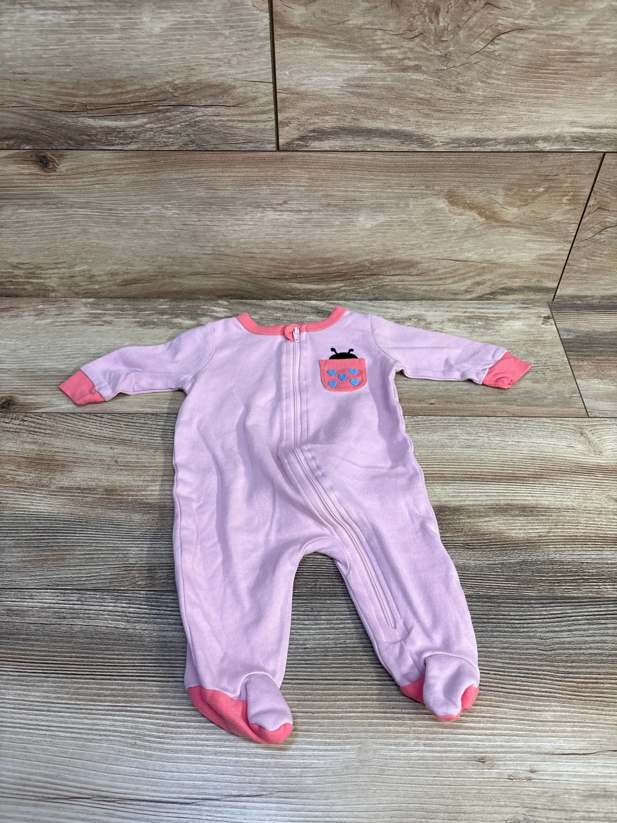 Front view of Koala Baby pink sleeper with long sleeves, covered feet, front zipper, and playful pocket print on wood background