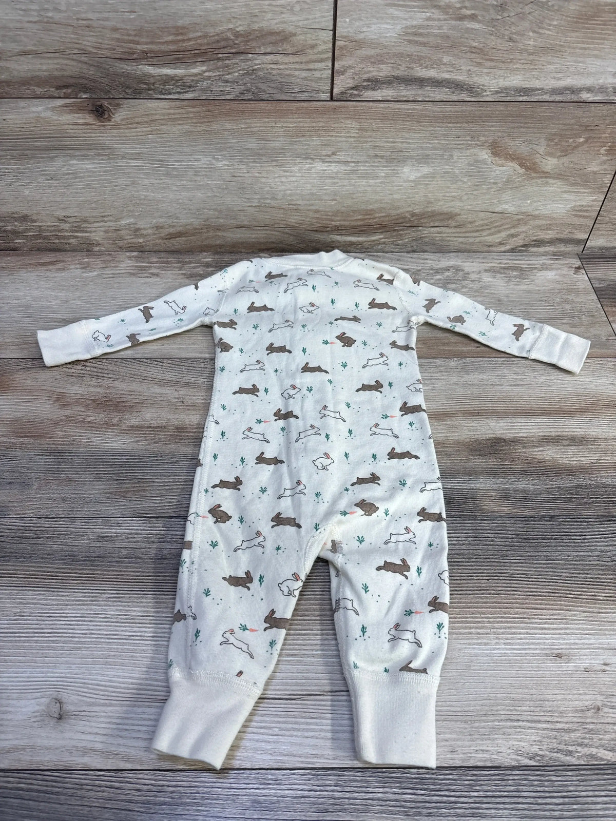 Top view of Hanna Andersson Bunny Footless Sleeper in pale yellow with allover bunny print on wood-grain background