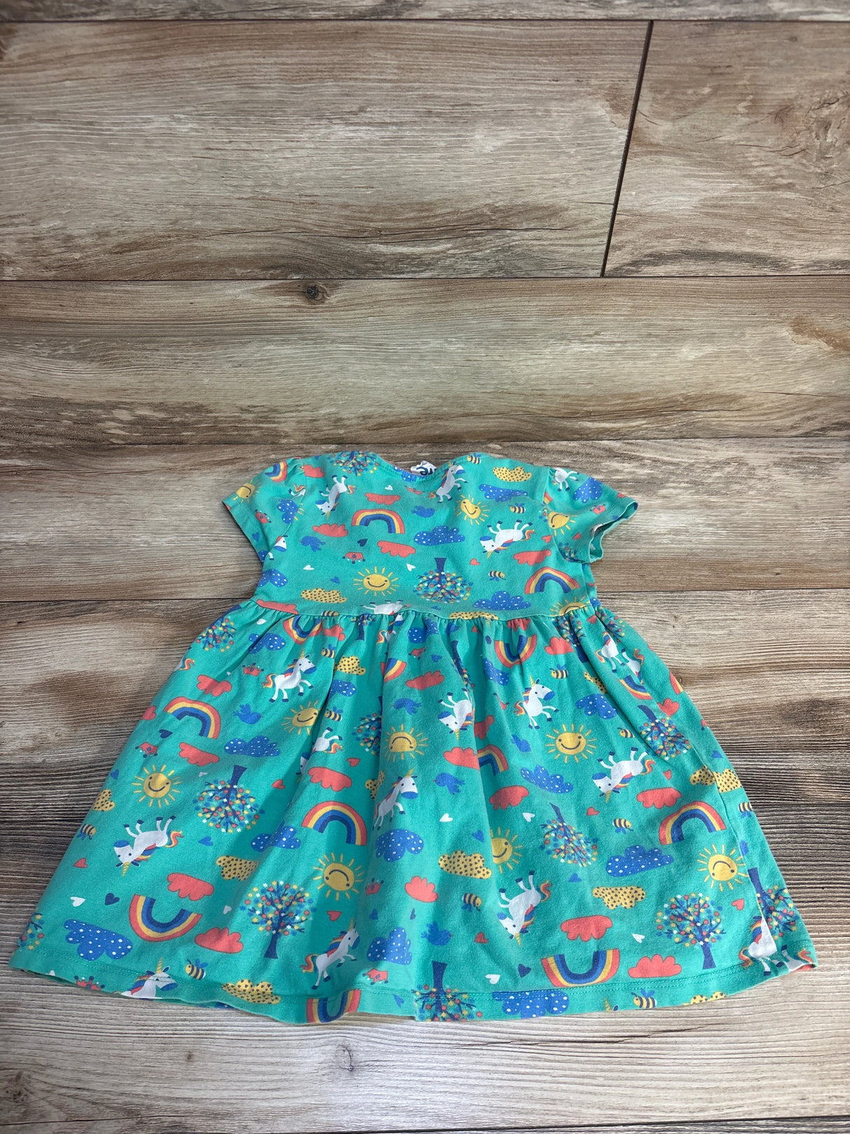 Teal toddler dress with unicorns, rainbows, and suns on wood floor