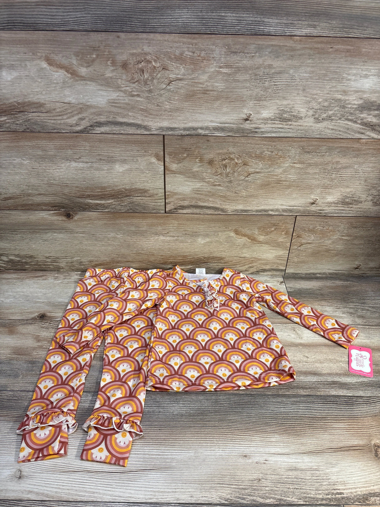 Flat lay of orange two-piece rainbow-print long-sleeve shirt and pants showcasing ricrac trim and ruffled pant cuffs on a wood background