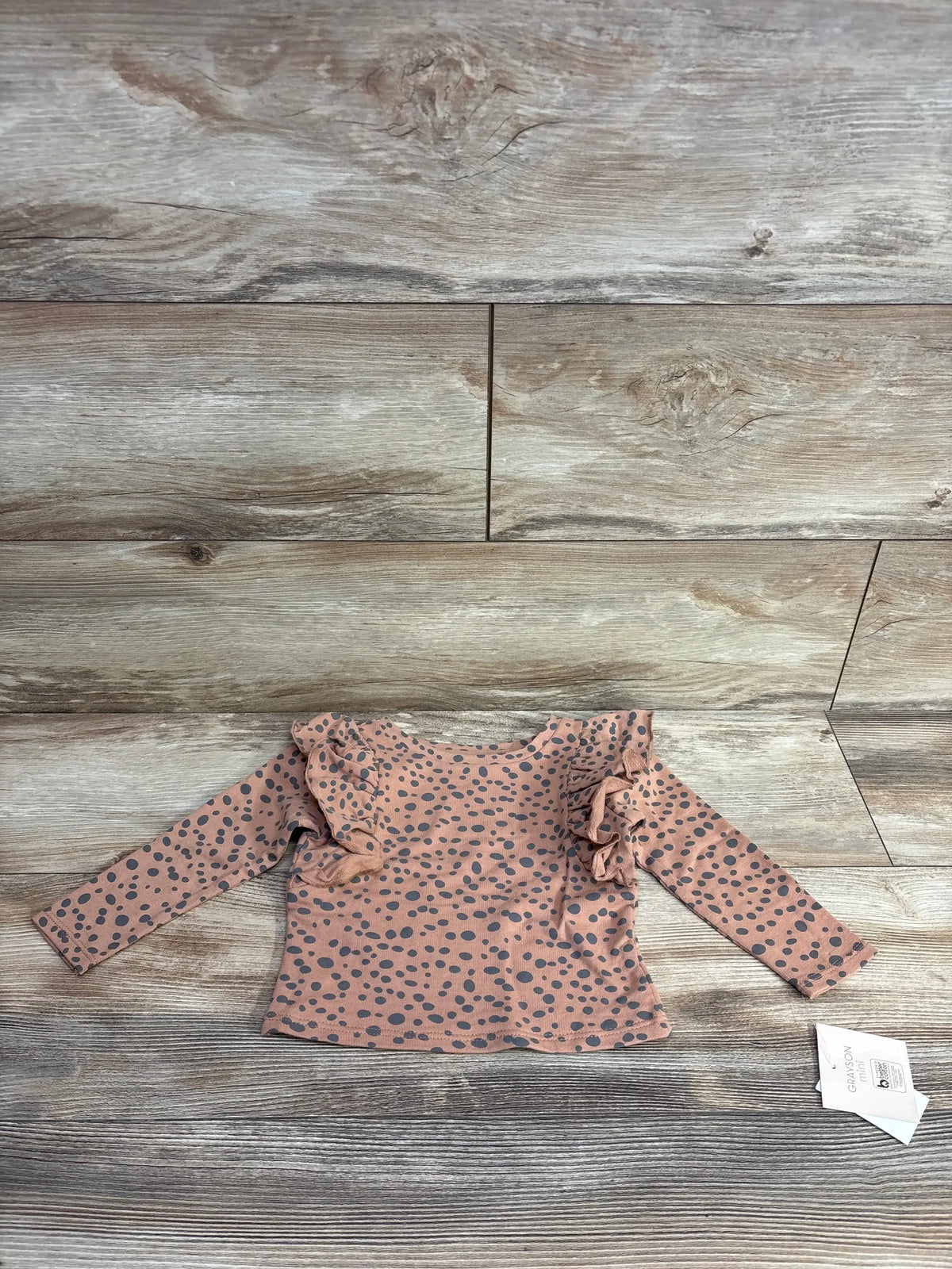 Front view of Grayson Mini ruffled polka dot top in brown, size 18M, with ruffle shoulders and black dots on wood floor