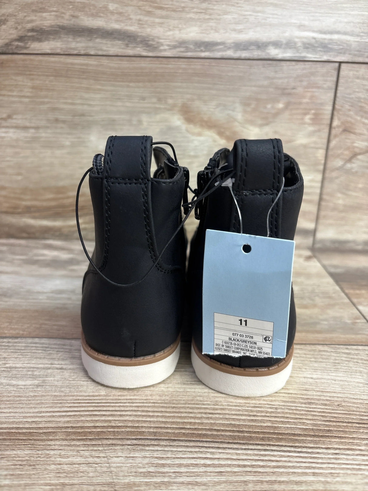 Back view of black toddler boots with white soles and size 11 tag on wooden floor