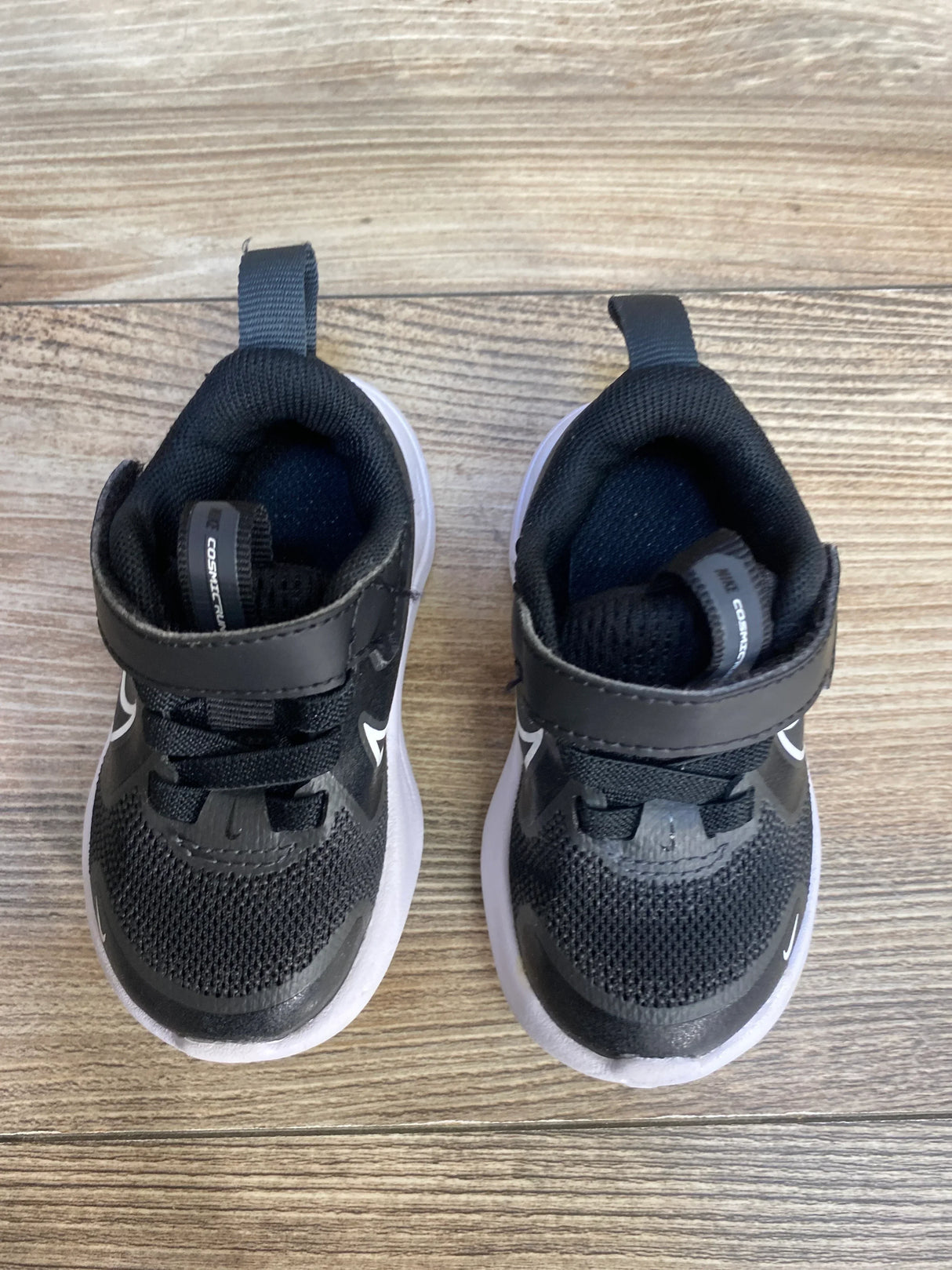 Top-down view of Nike Cosmic Runner TD 'Black White' toddler sneakers showcasing Velcro strap and white sole on wood floor