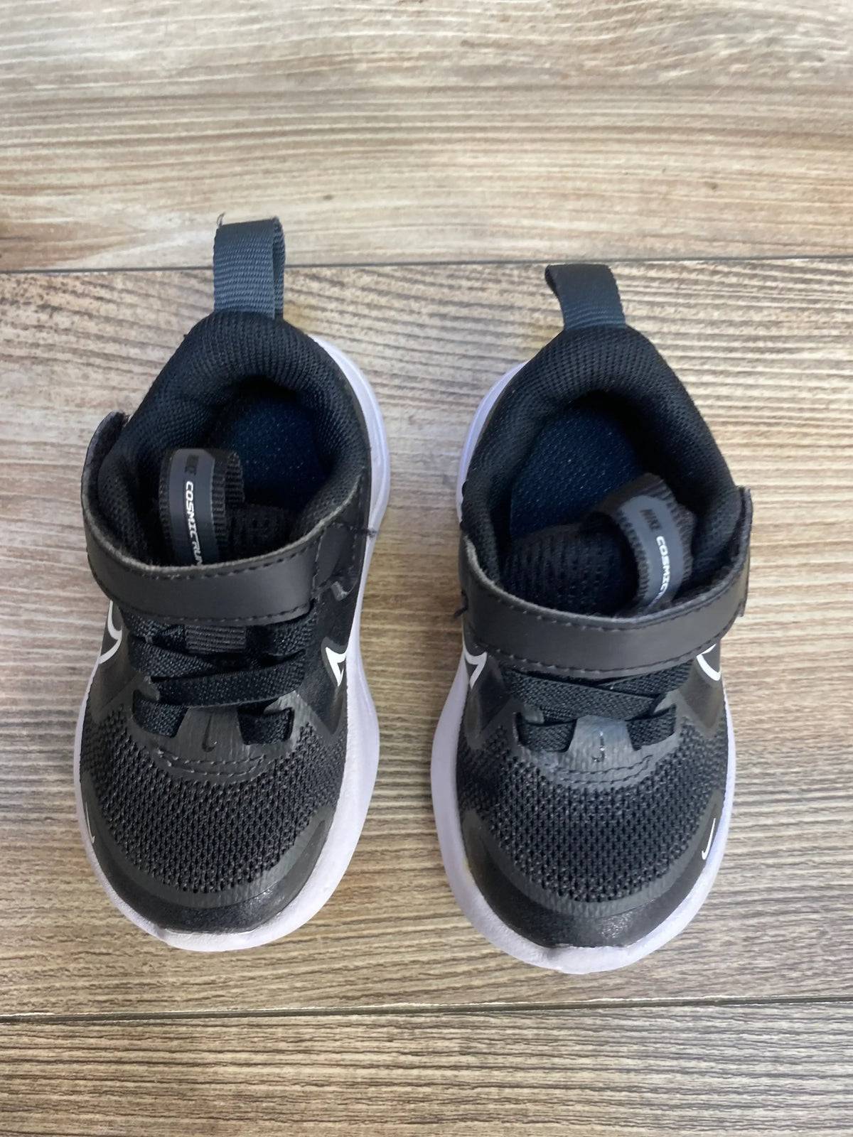 Top-down view of Nike Cosmic Runner TD 'Black White' toddler sneakers showcasing Velcro strap and white sole on wood floor