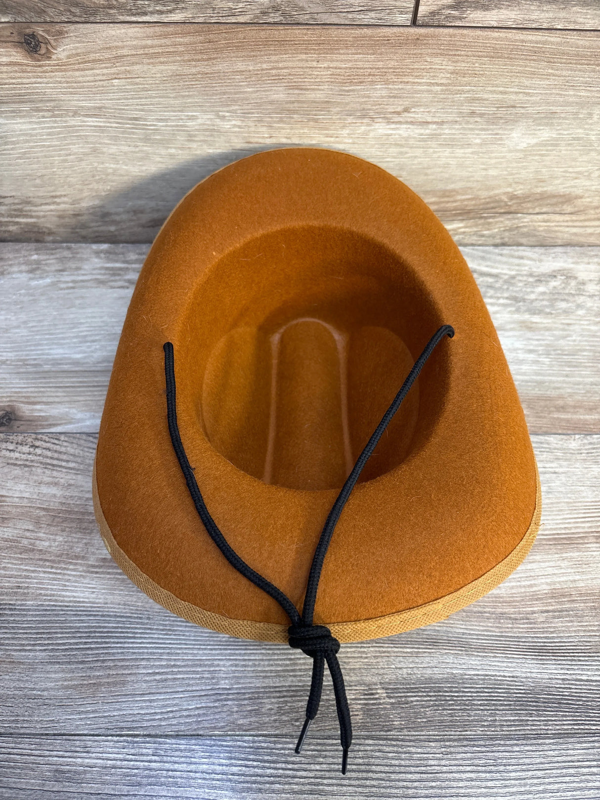 Brown felt cowboy hat with black chin strap on wooden surface