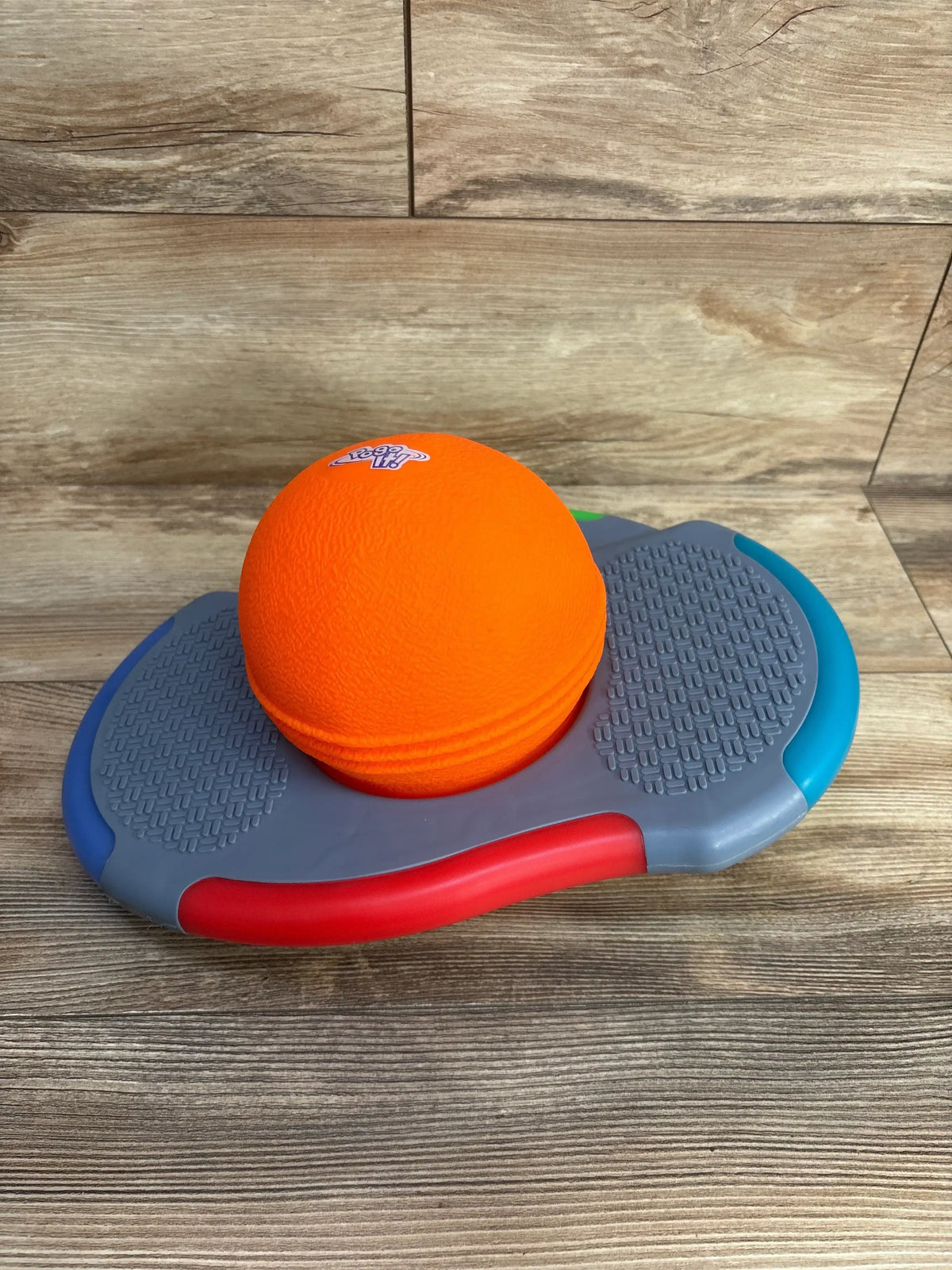 Angled top view of Little Tikes Pogo It showcasing bright orange ball, textured gray footpads, and red and blue trim on wood floor