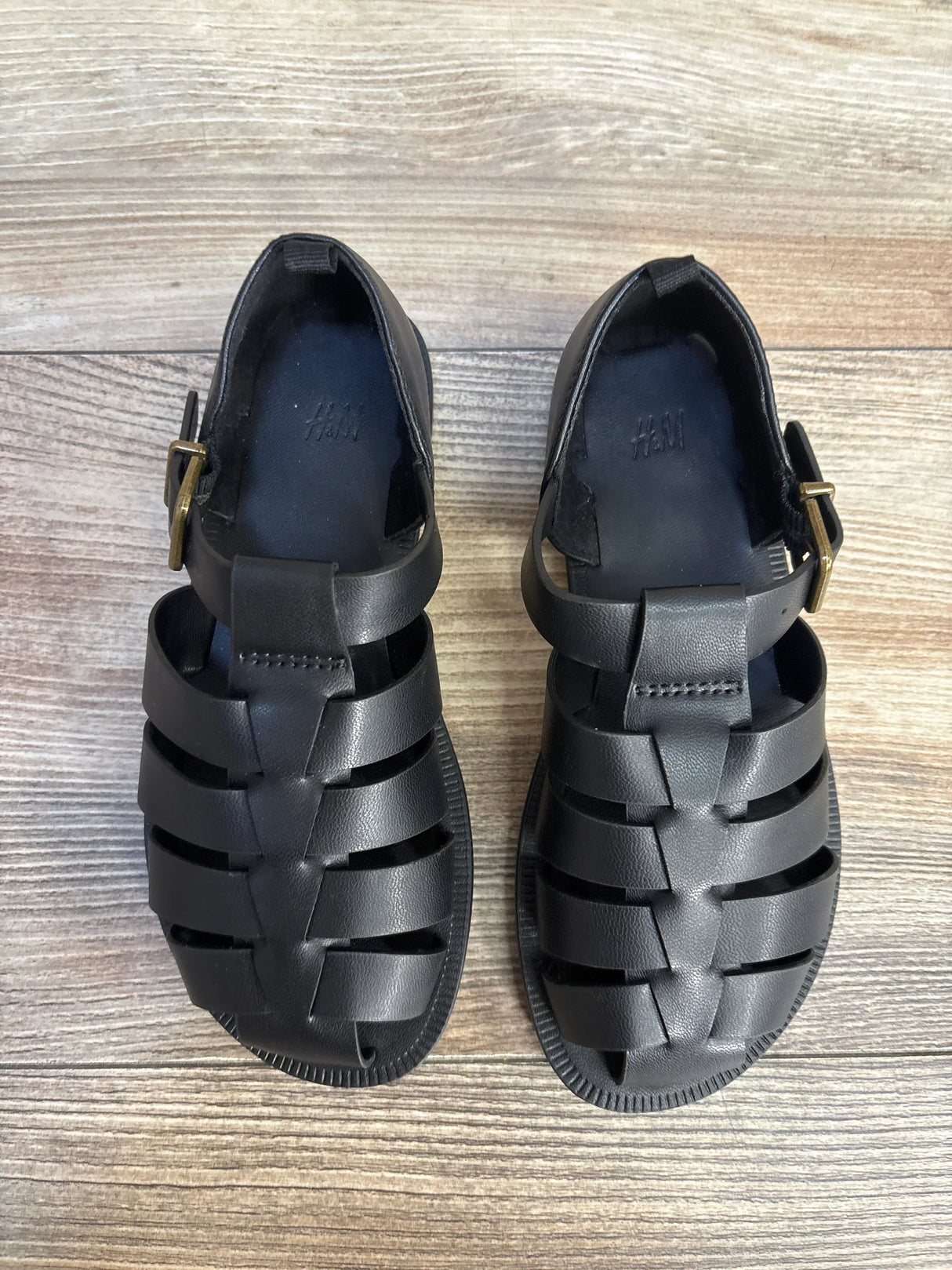 Pair of black toddler sandals with buckles on wood floor, gently used kids shoes