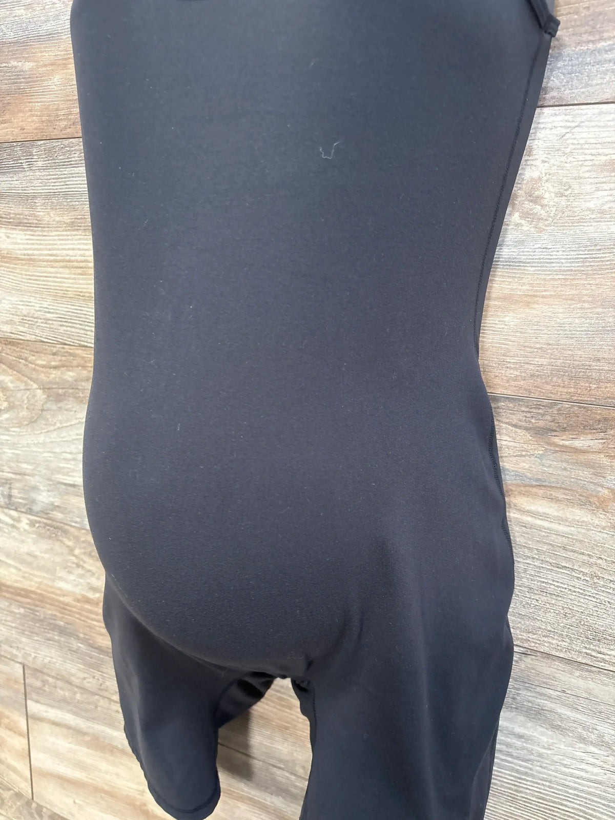 Front view of black Isabel maternity active romper showcasing its sleeveless design, fitted belly, and mid-thigh shorts on wood background