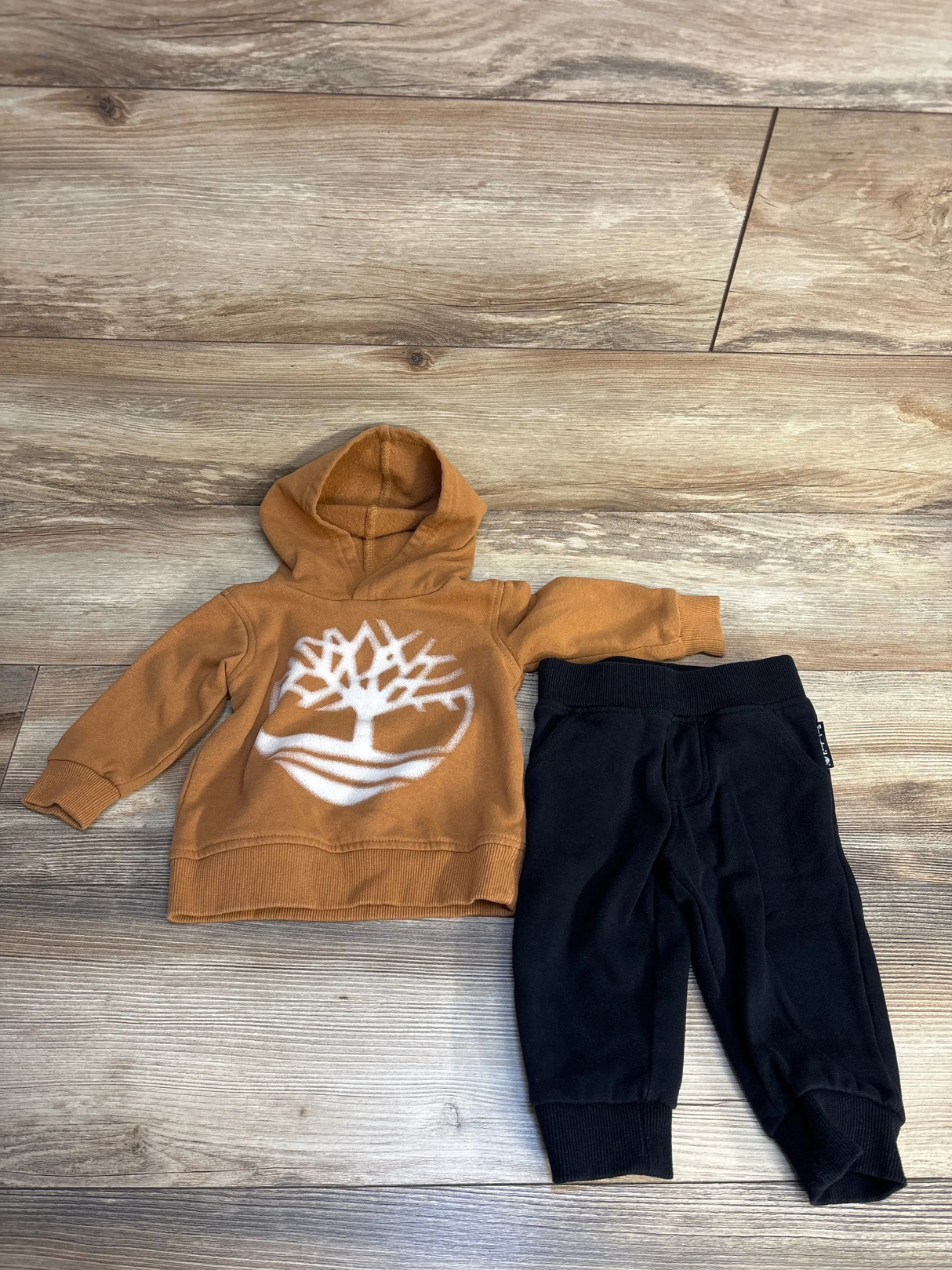 Toddler outfit with brown tree print hoodie and black pants on wood background