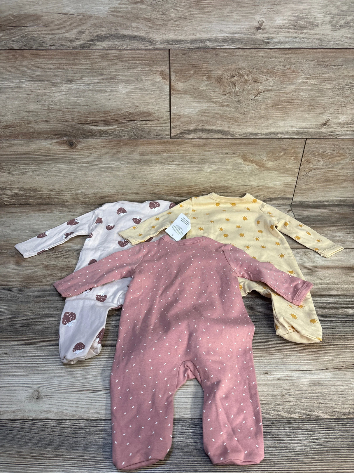 Three baby footed sleepers in pink, white, and yellow with cute patterns on wood floor