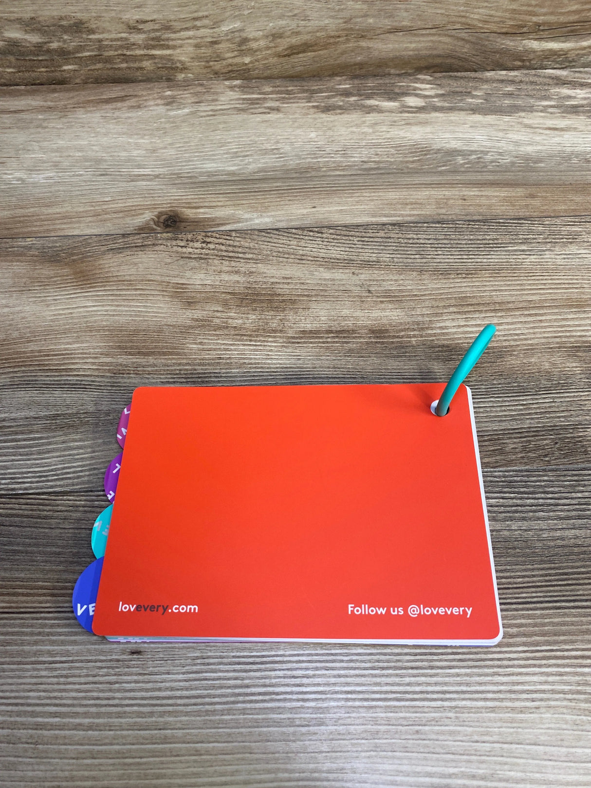 Orange baby flashcards with tabs and blue ring on wooden table from Lovevery