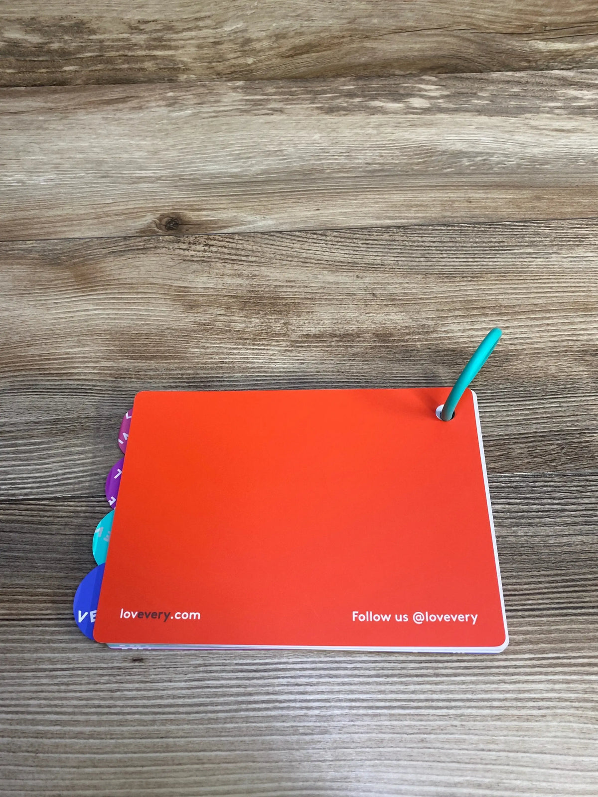 Top-down view of Lovevery The Senser Play Guide showcasing its orange cover, colored section tabs, and teal binding ring on a wooden table