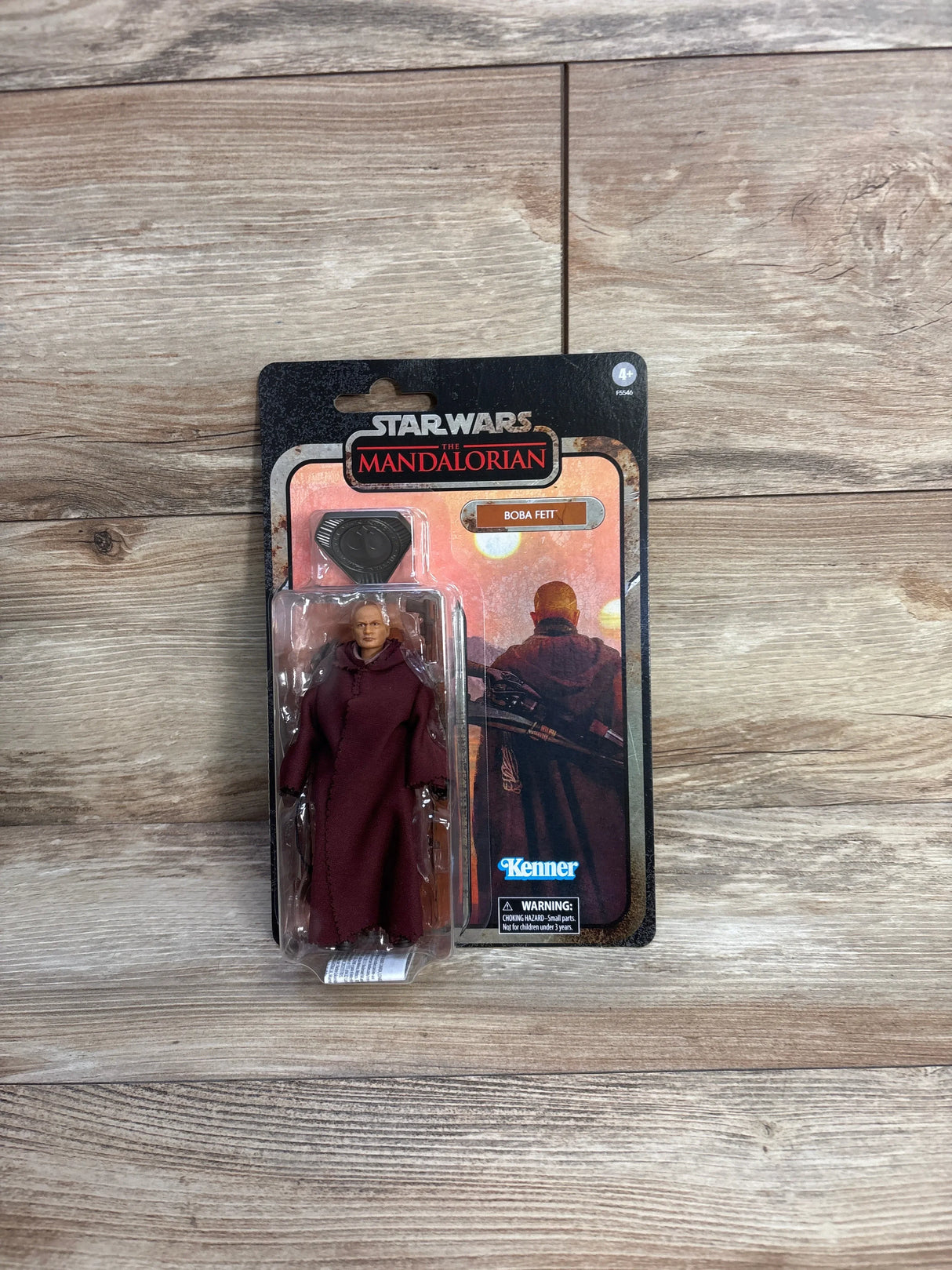 Front view of Star Wars The Mandalorian Boba Fett Kenner action figure in sealed blister card packaging on wood plank floor